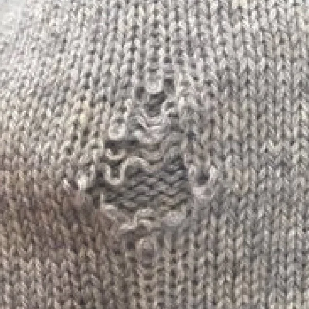 Close-up of a beige or light gray knitted fabric with a small ripped hole.