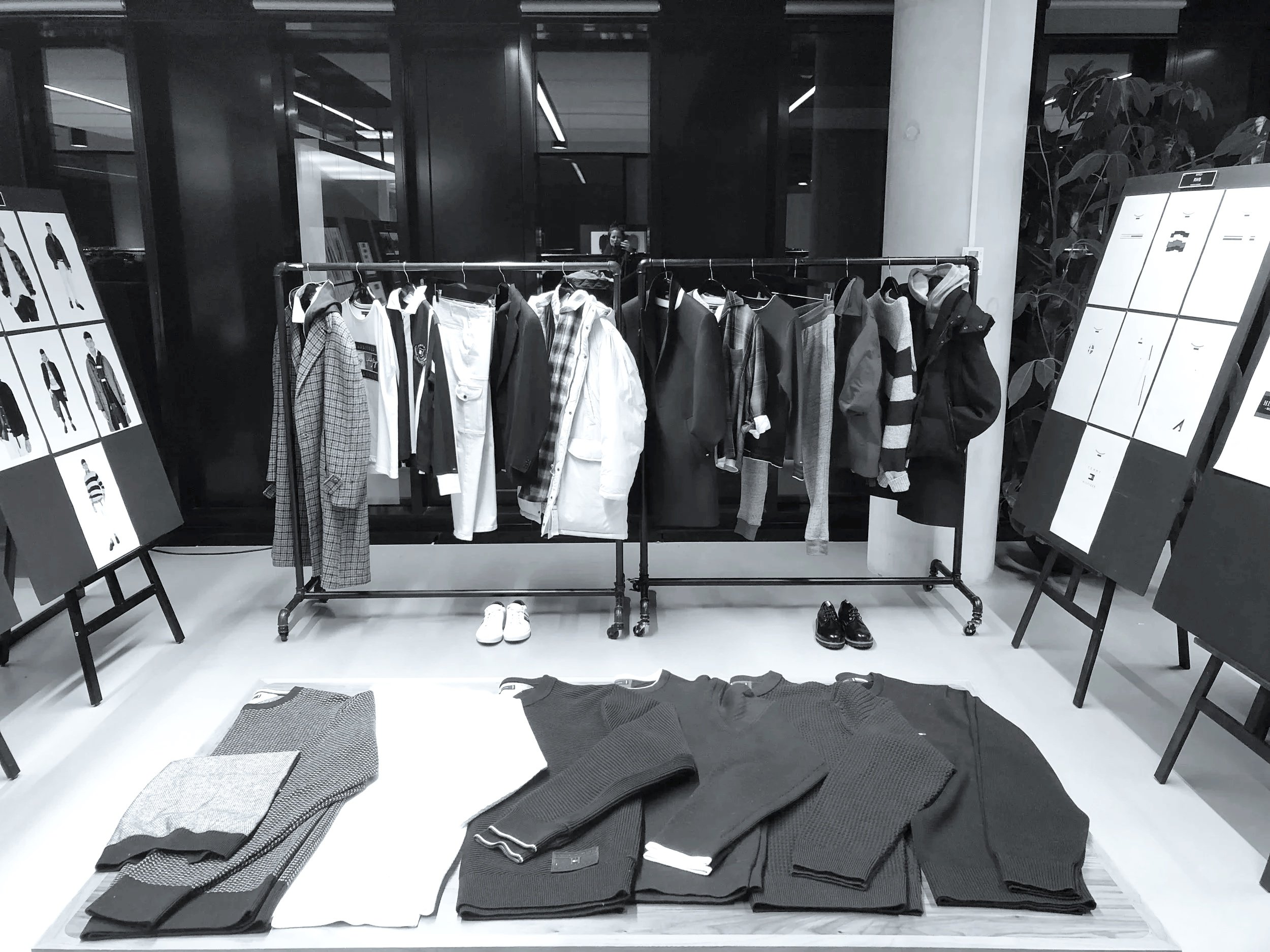 clothing display with jackets, shirts, and sweaters on a rack and folded clothing on a table in a retail store
