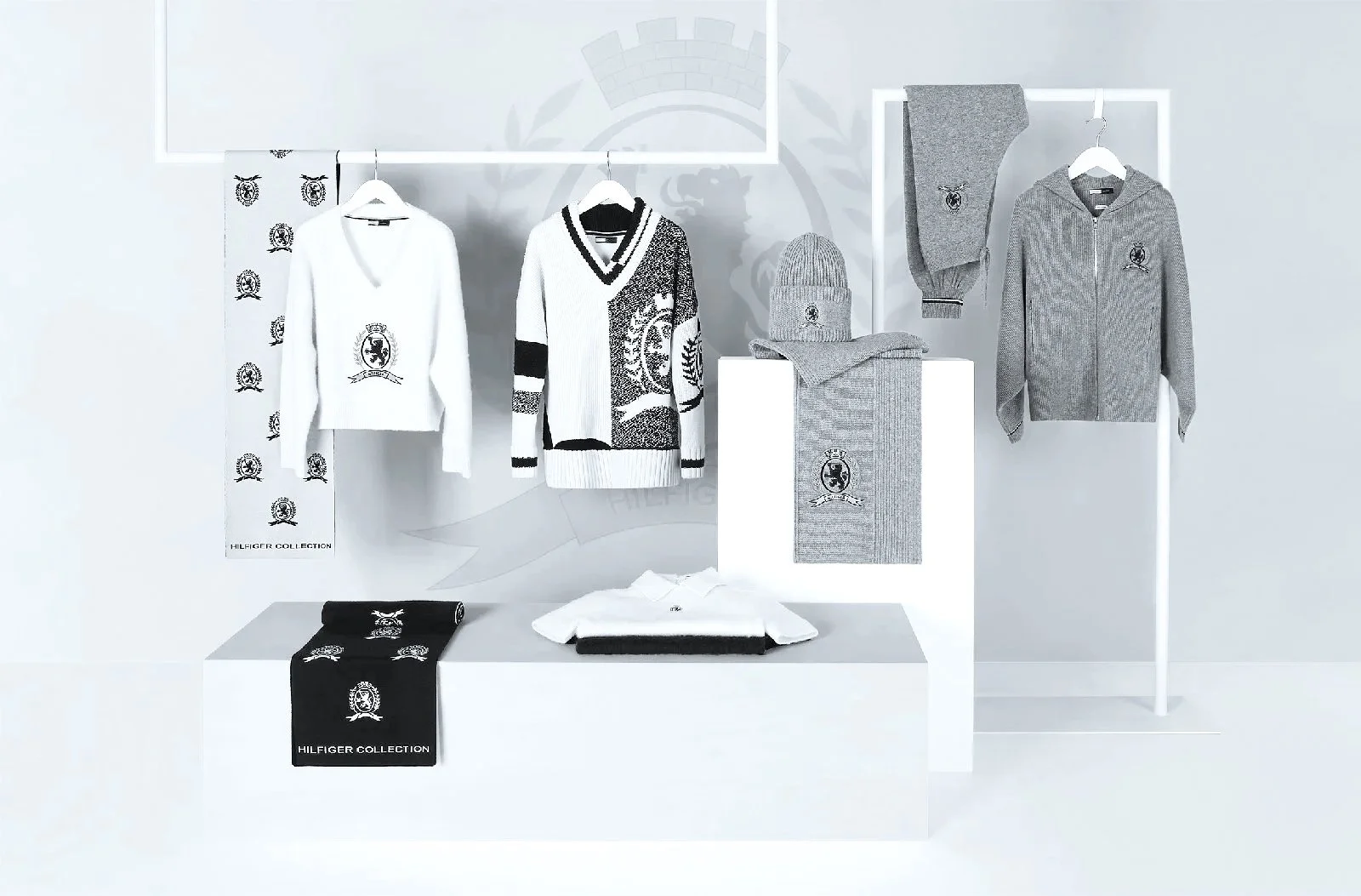 Display of clothing items including sweaters, shirts, a beanie, and scarves, all branded with the Hilfiger Collection logo, arranged on shelves and hangers in a retail setting.