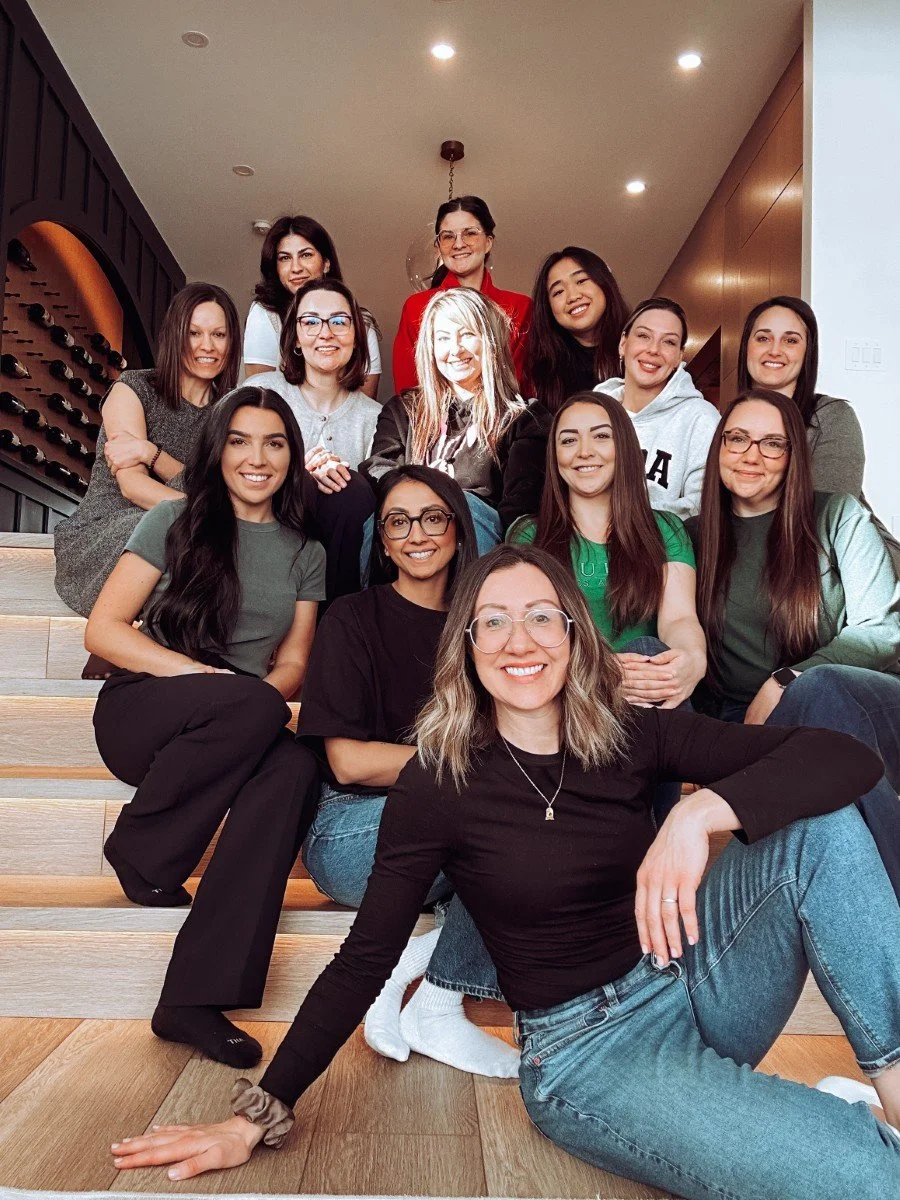 A group of women sitting on a set of stairs leaning inwards and smiling at the camera.