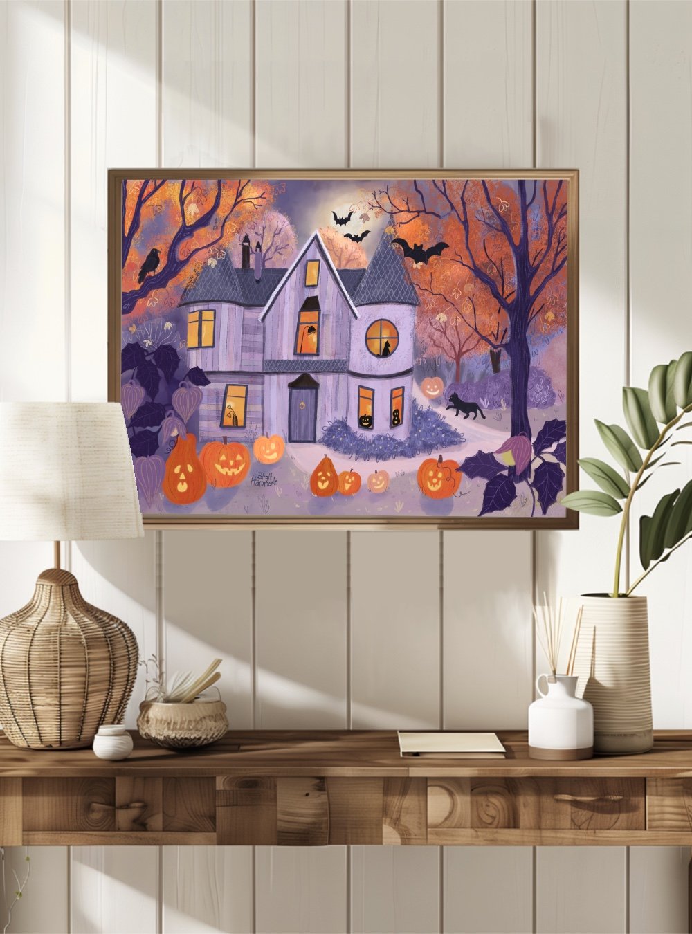 Mockup of cosy Halloween house art print in gold frame above dining table with tea cup and flowers