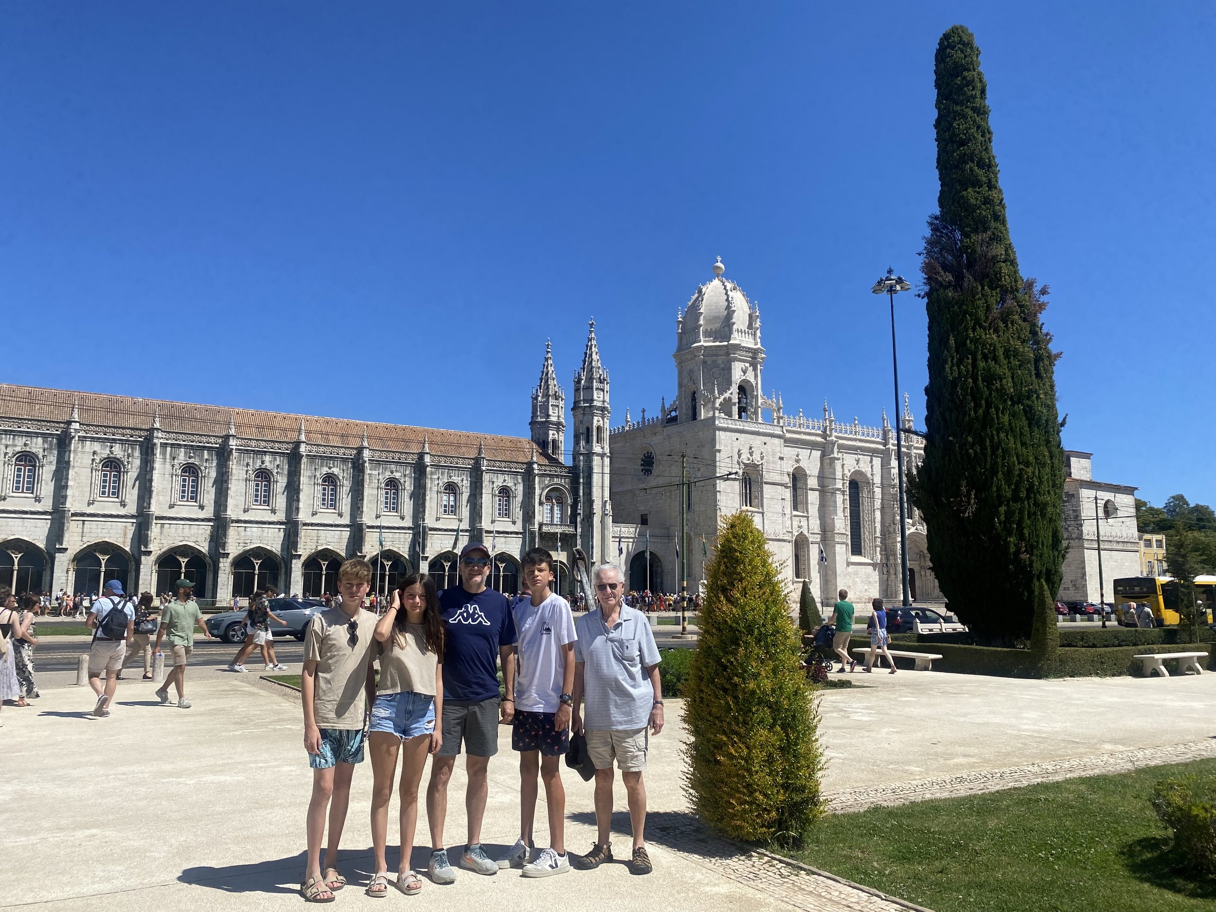 Grupo de personas posando frente a un edificio histórico en un día soleado, con cielo azul y árboles verdes alrededor, gracias a un viaje personalizado realizado por Bomvento.
