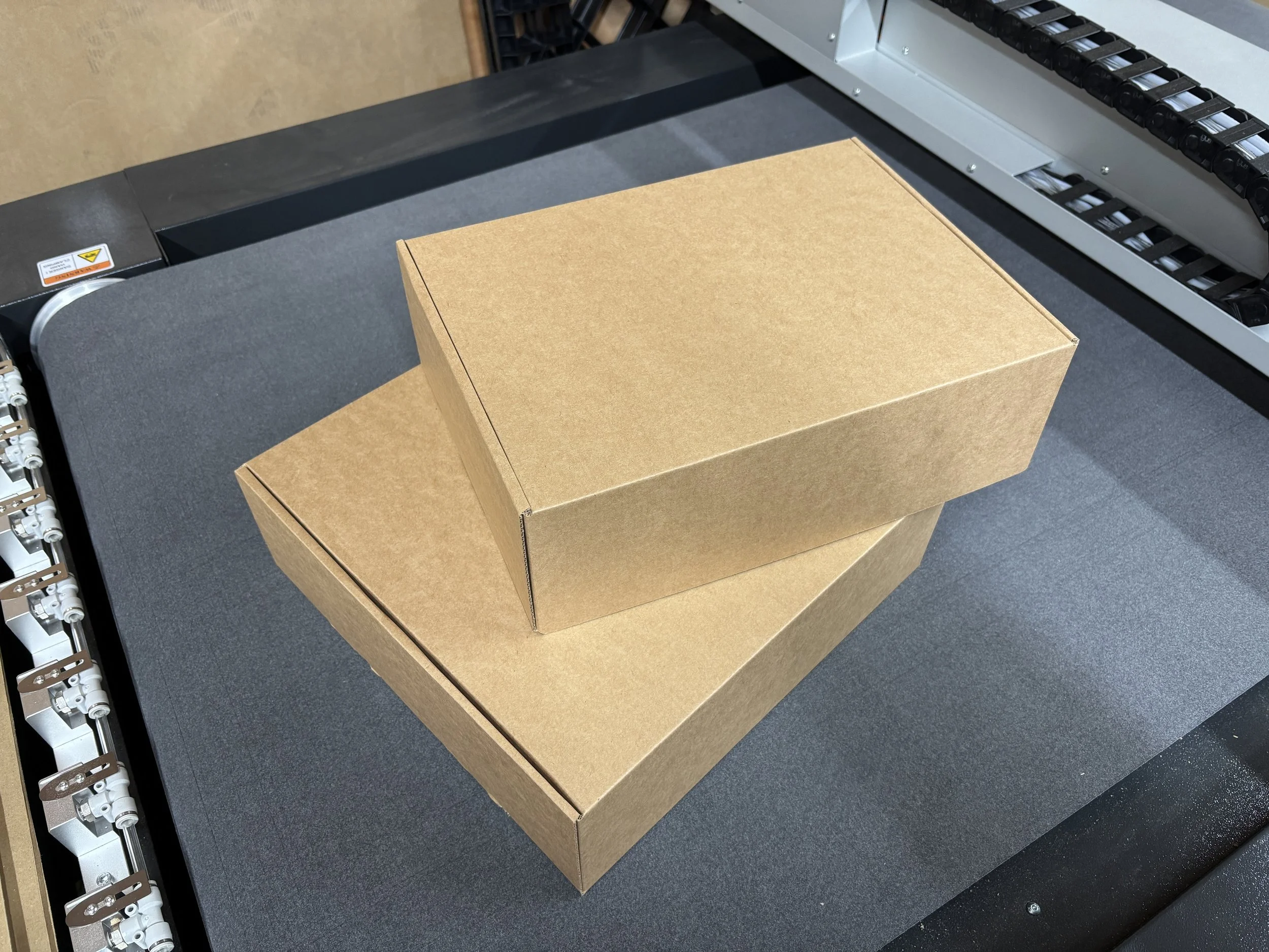 Two plain cardboard boxes, one stacked on top of the other on a conveyor belt or sorting machine.