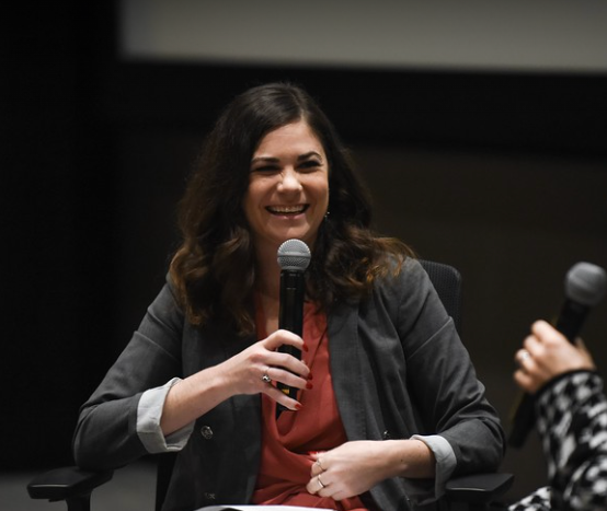 Sara Wigal smiling and holding a microphone during a discussion or interview.