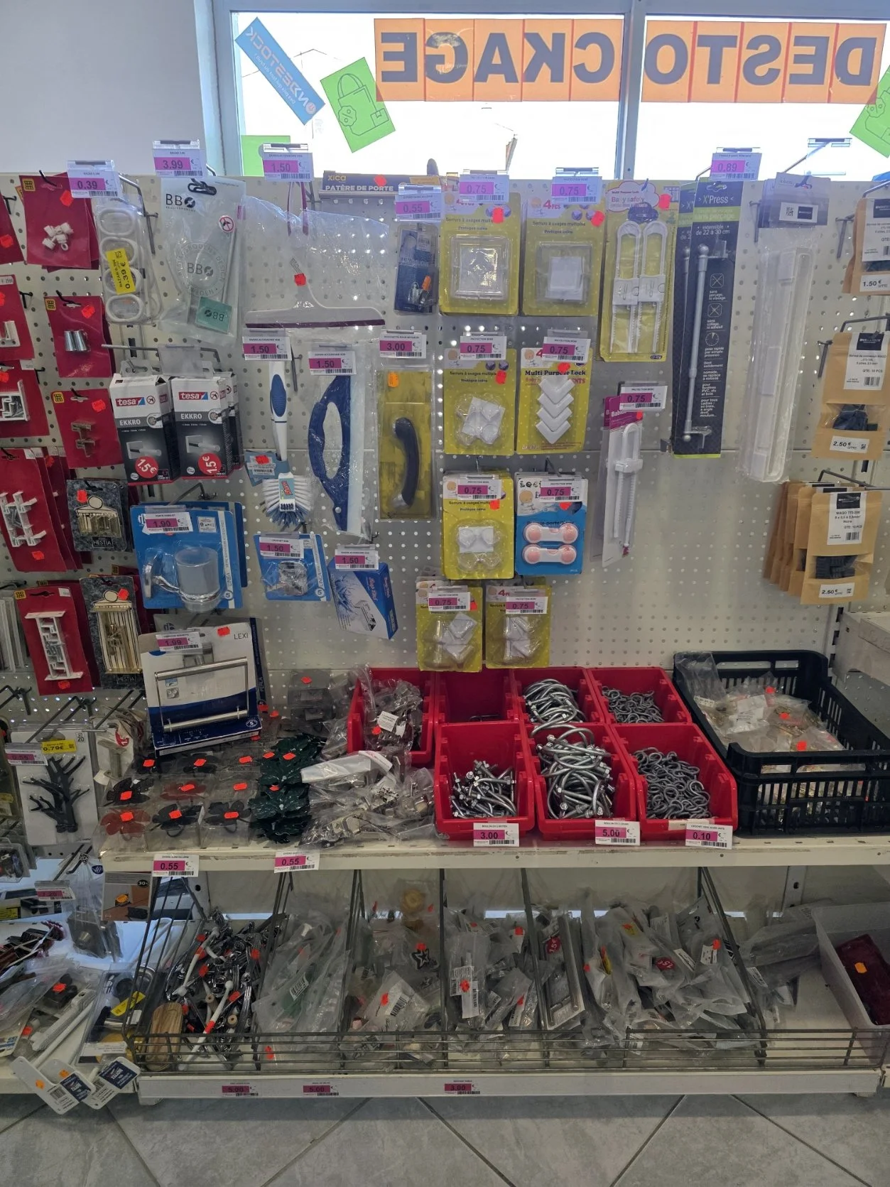 Rayonnage dans une quincaillerie avec divers accessoires de fixation, vis, crochets, et autres petits outils pour le bricolage.