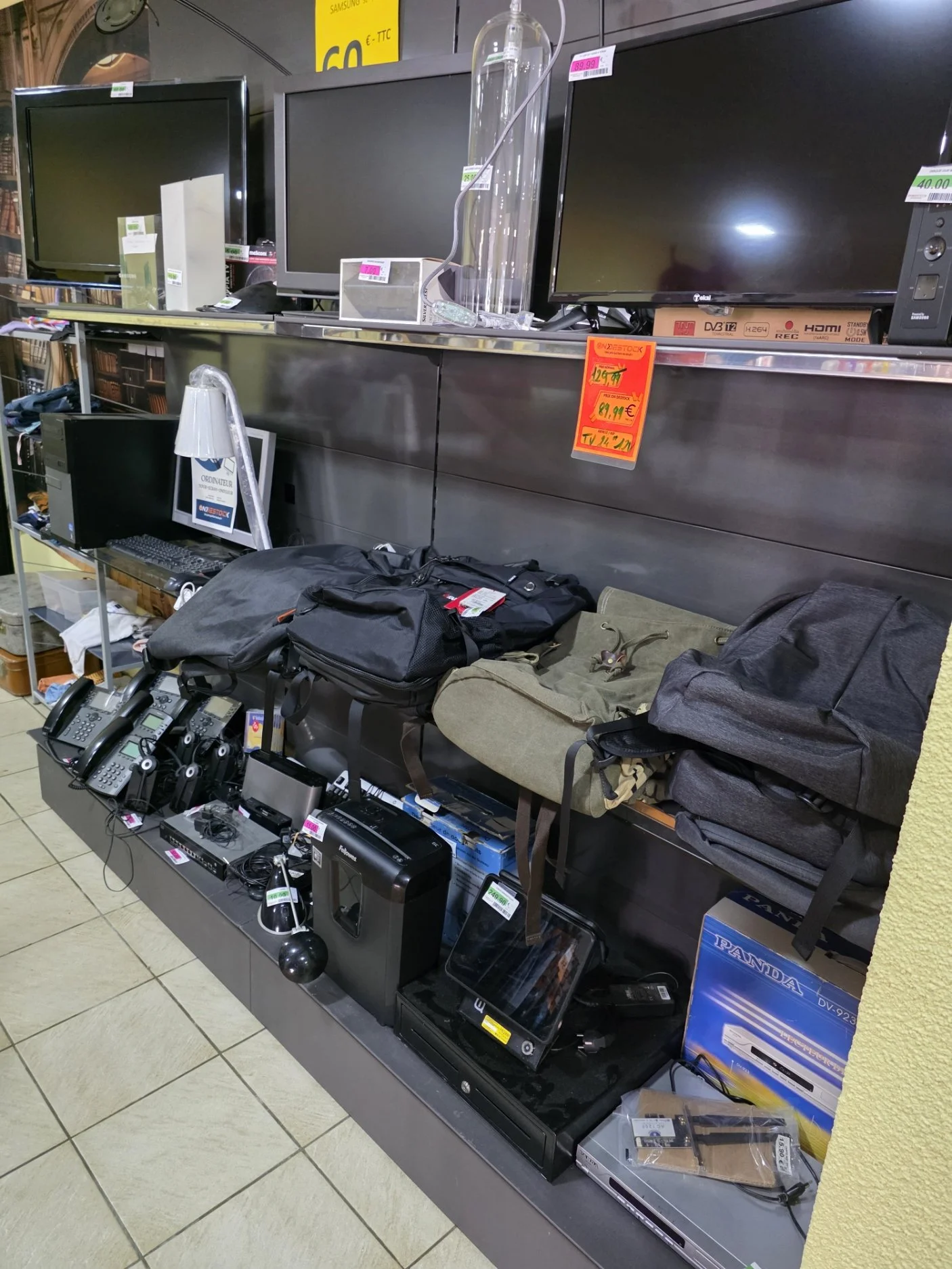 Électronique en vente dans un magasin d'occasion, avec téléviseurs, ordinateurs, téléphones, accessoires et autres appareils électroniques sur des étagères.