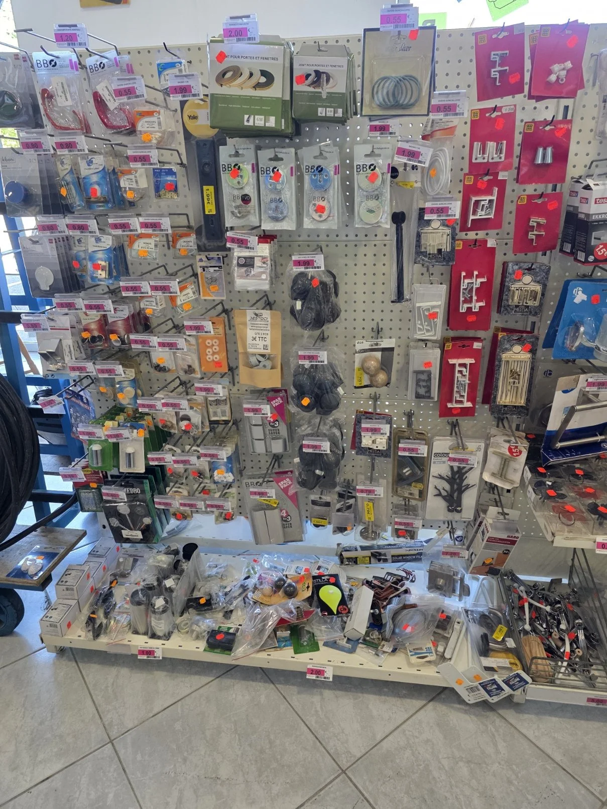 Une étagère de quincaillerie dans un magasin, contenant des câbles, des clips, des poignées de porte, des serrures, des décorations et d'autres petits accessoires.