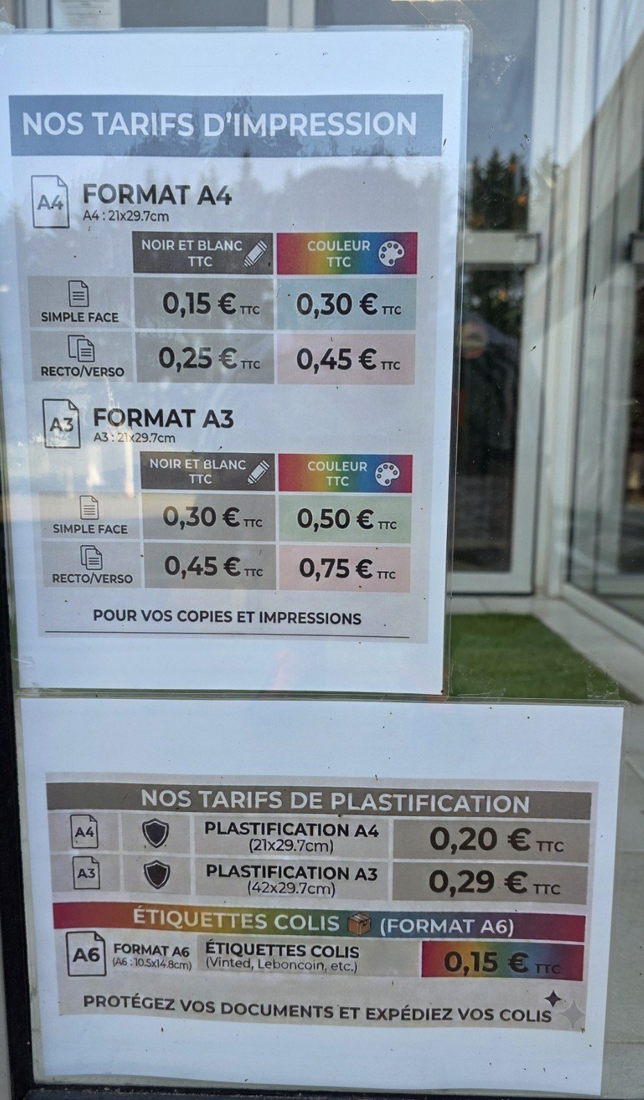 Tarifs d'impression et de plastification affichés dans une vitrine d'imprimerie.