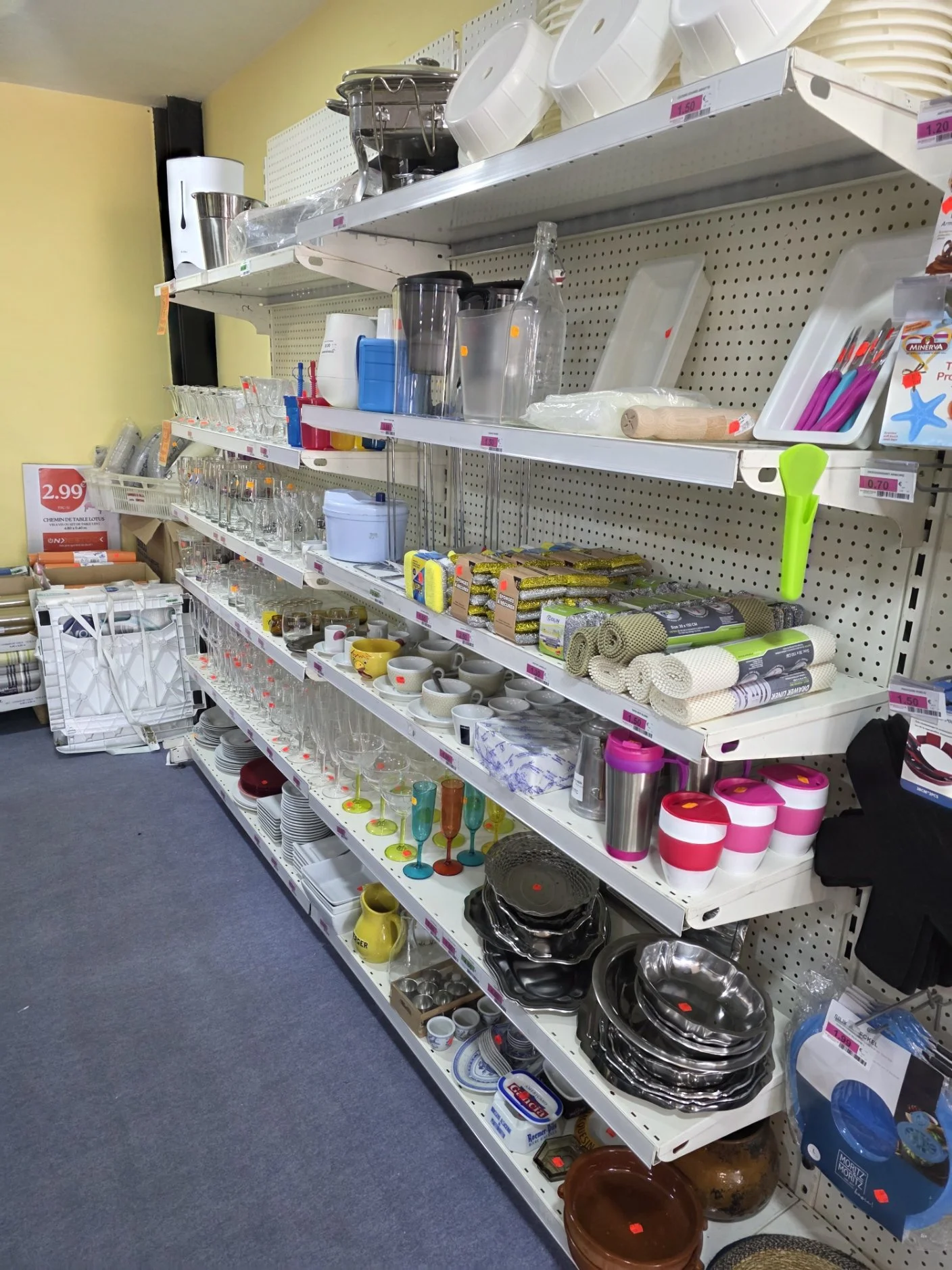 Rayonnage dans un magasin d'articles de cuisine avec vaisselle, ustensiles, verres, plats, couverts, tapis de bain, et autres accessoires.