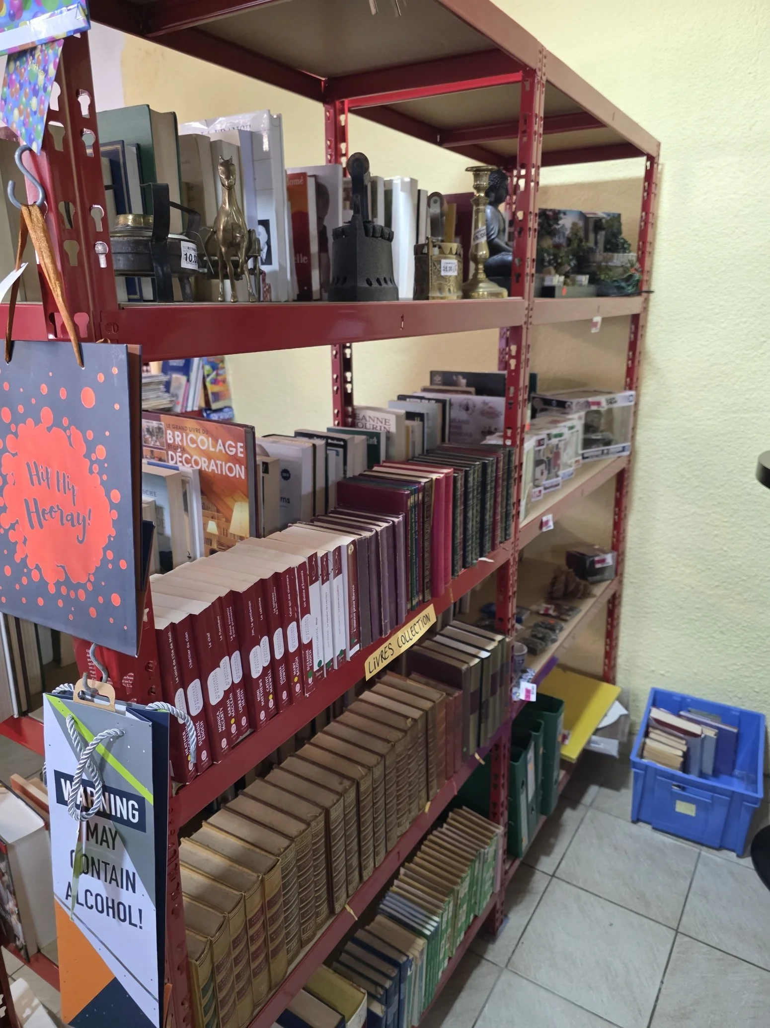 Une étagère colorée contenant des livres, des objets décoratifs, et un panneau indiquant des conseils de sécurité. Le sol est en carrelage.