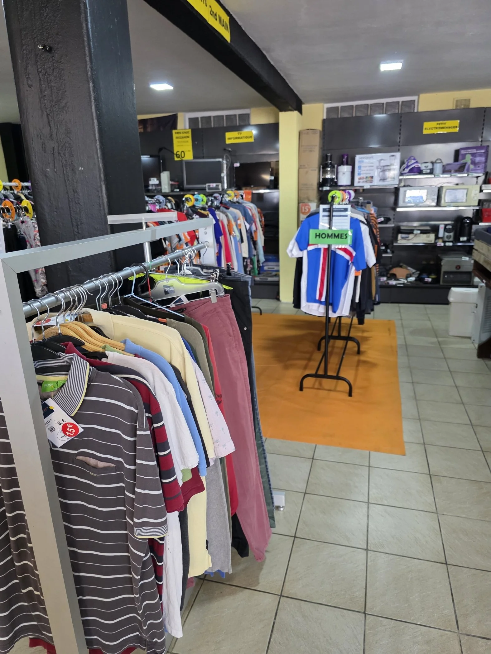 Rayonnage avec vêtements pour hommes, vêtements colorés, section pour hommes dans un magasin. Signes en français et panneaux de prix.