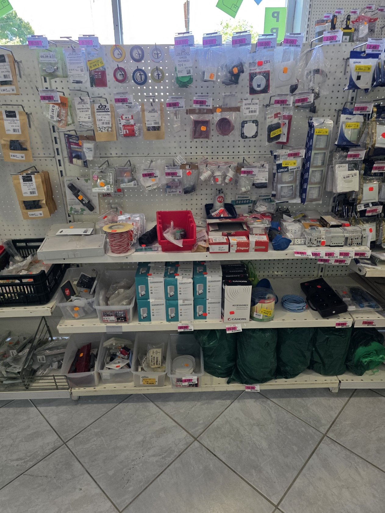 Rayonnage de matériel électrique et accessoires dans un magasin, comprenant des prises électriques, câbles, plombs, et autres composants électroniques.