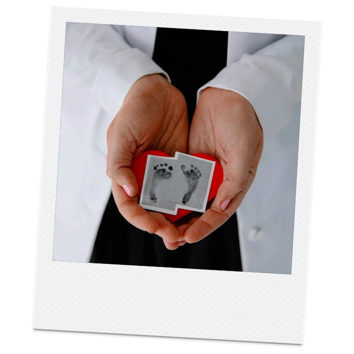 Person wearing a white coat holding a small photo of baby footprints.