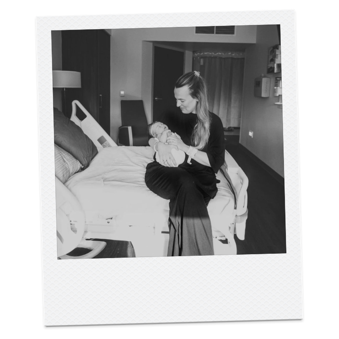 A woman sitting on a hospital bed holding a newborn baby in a hospital room.