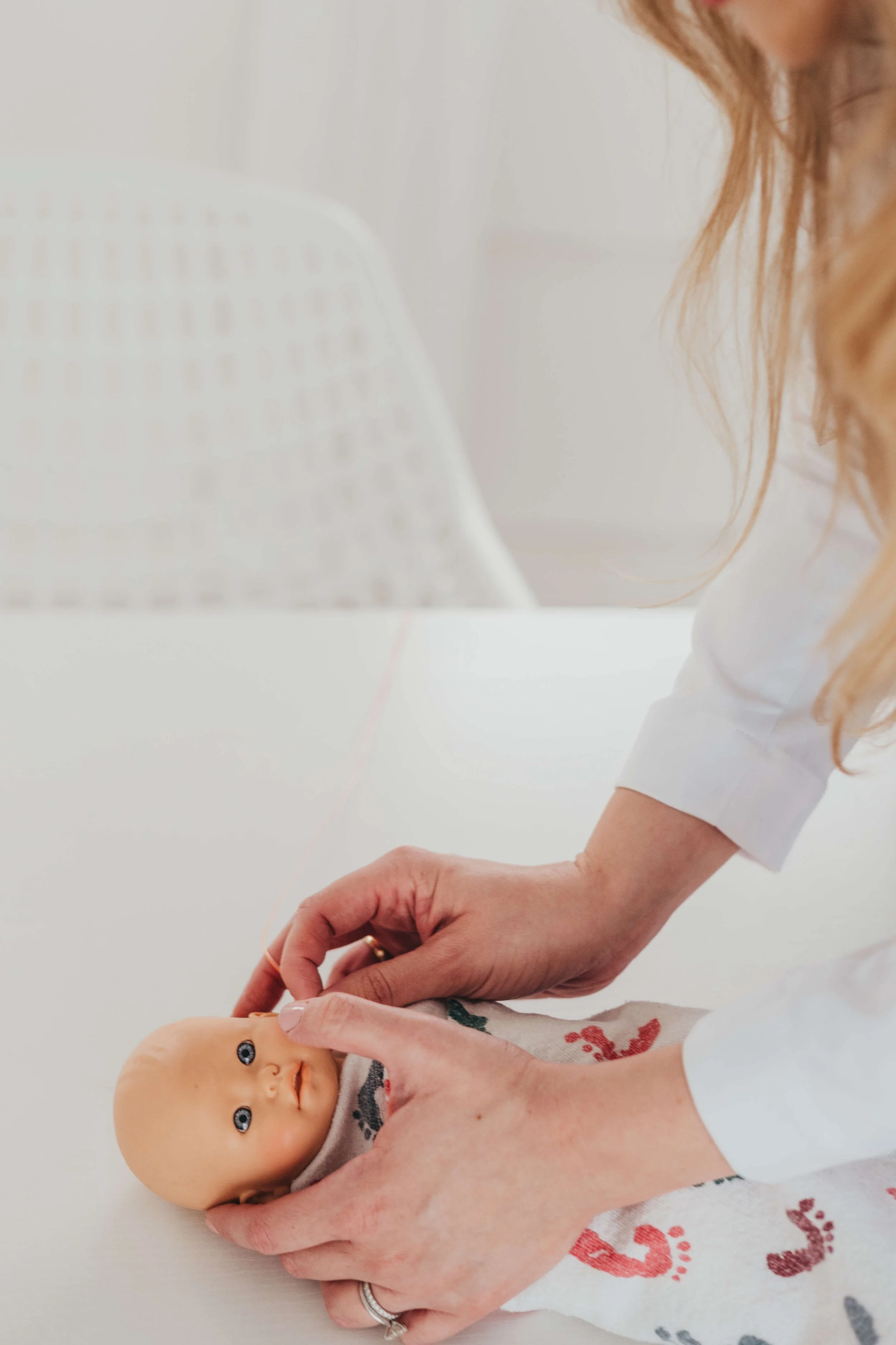 A woman holding a newborn baby with blue eyes, wrapped in a blanket, in a bright, minimal setting.