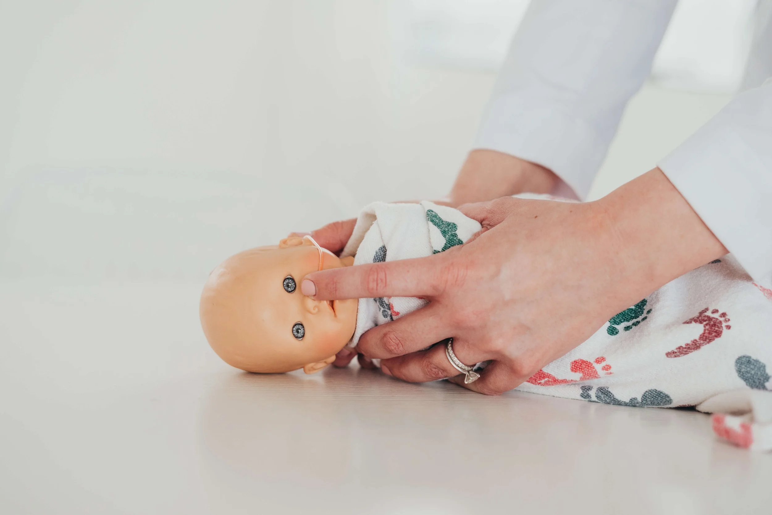 Person holding a baby doll with a white blanket that has colored prints, on a white surface.