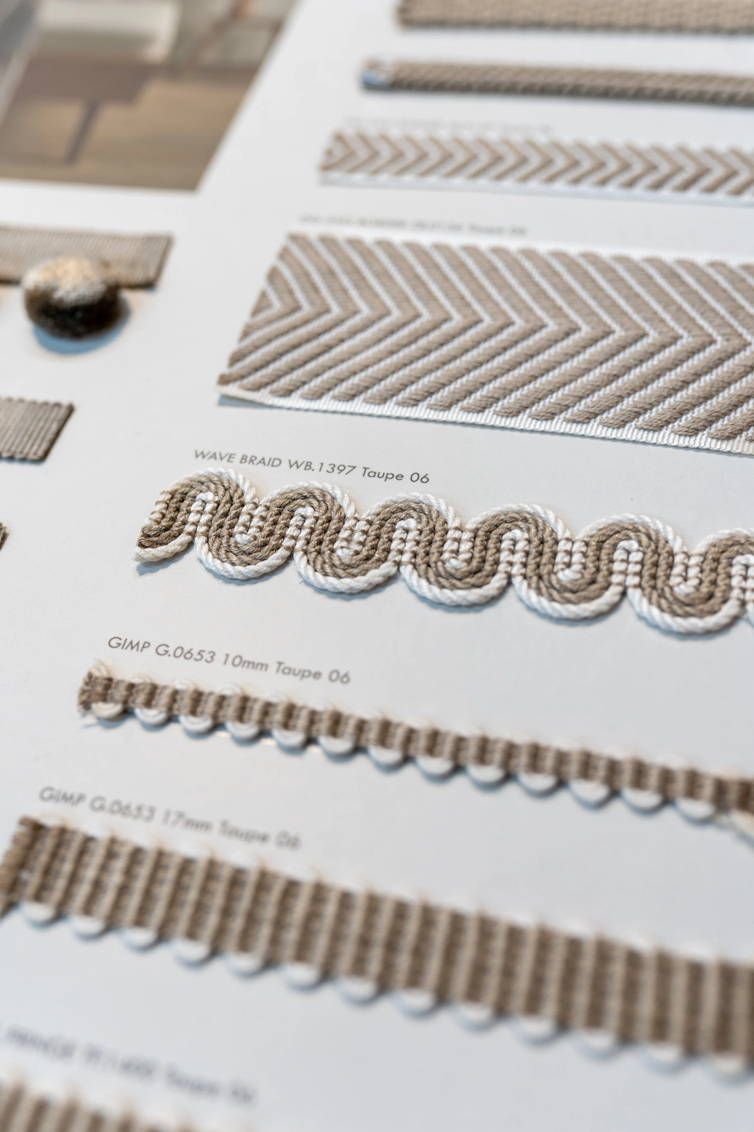 Close-up of a fabric sample book showing various beige textile trims and cords, with detailed textures and patterns.
