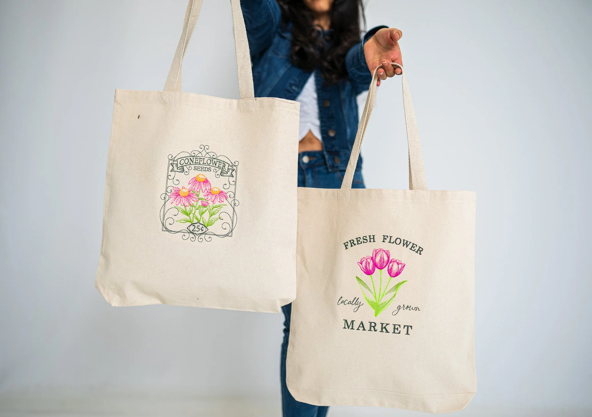 Person holding two reusable tote bags with floral illustrations and market text