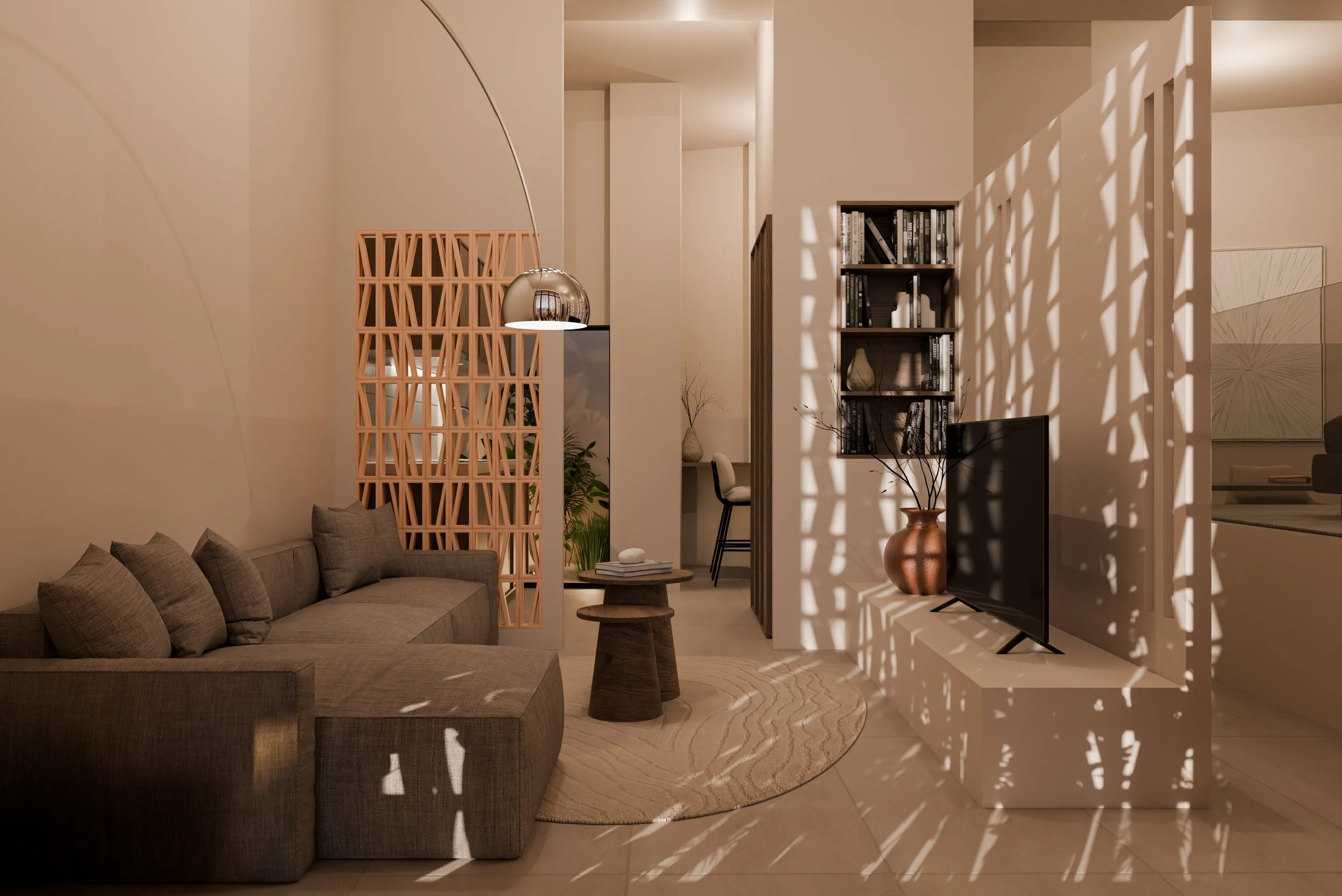 Living room with a gray sectional sofa, a round wooden coffee table, a textured beige rug, a mounted flat-screen TV, a bookshelf, a large copper vase with branches, and sunlight creating patterned shadows on the wall and furniture.