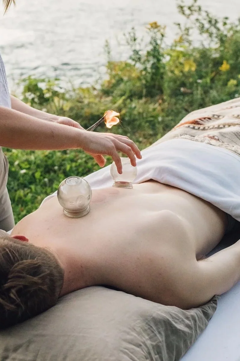 Person receiving an outdoor glass cupping therapy session near a lake, with a candle held nearby.