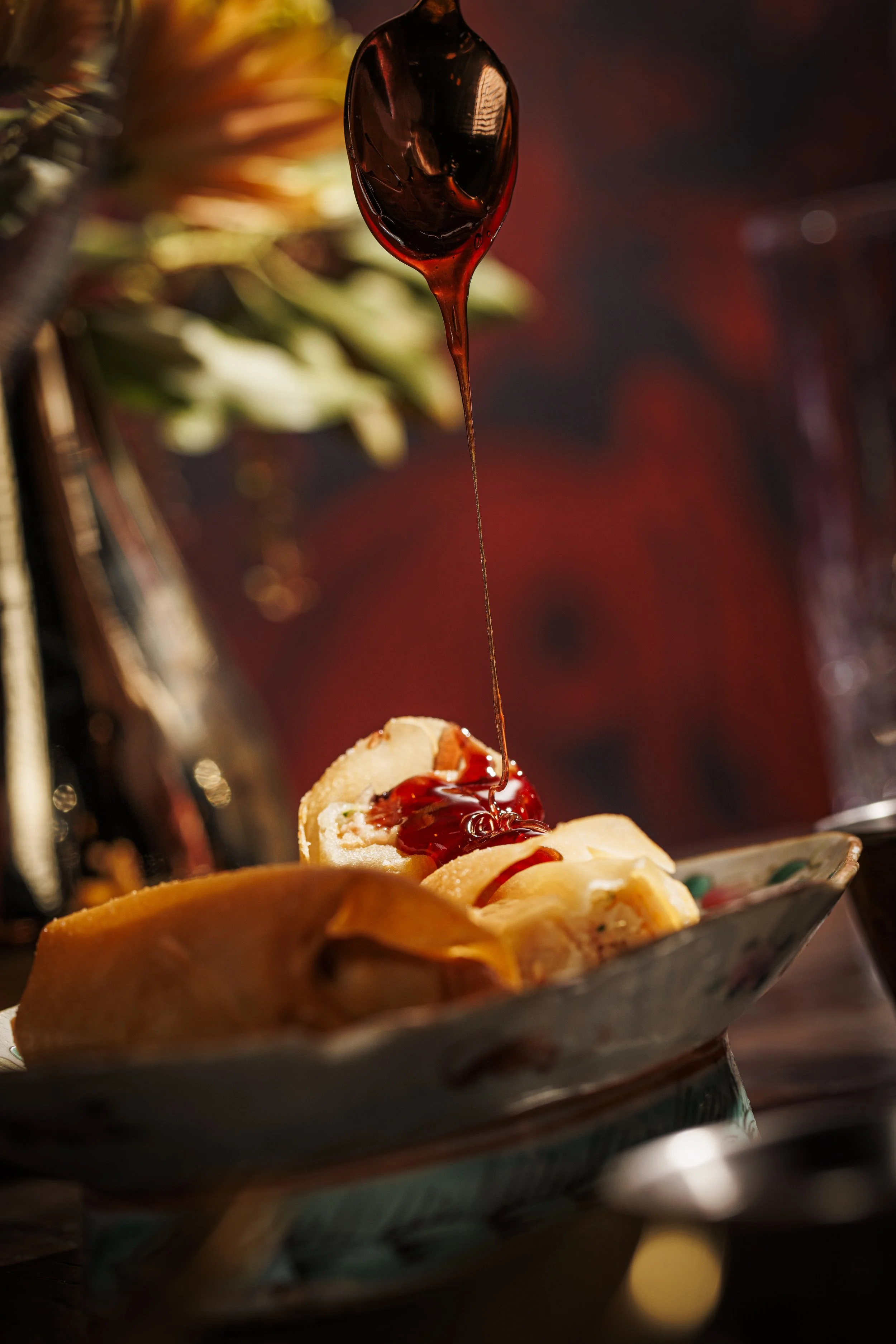 A spoon pouring Pomegranate Sweet and Sour sauce over a plate of Shrimp and Pork Air Eggrolls.