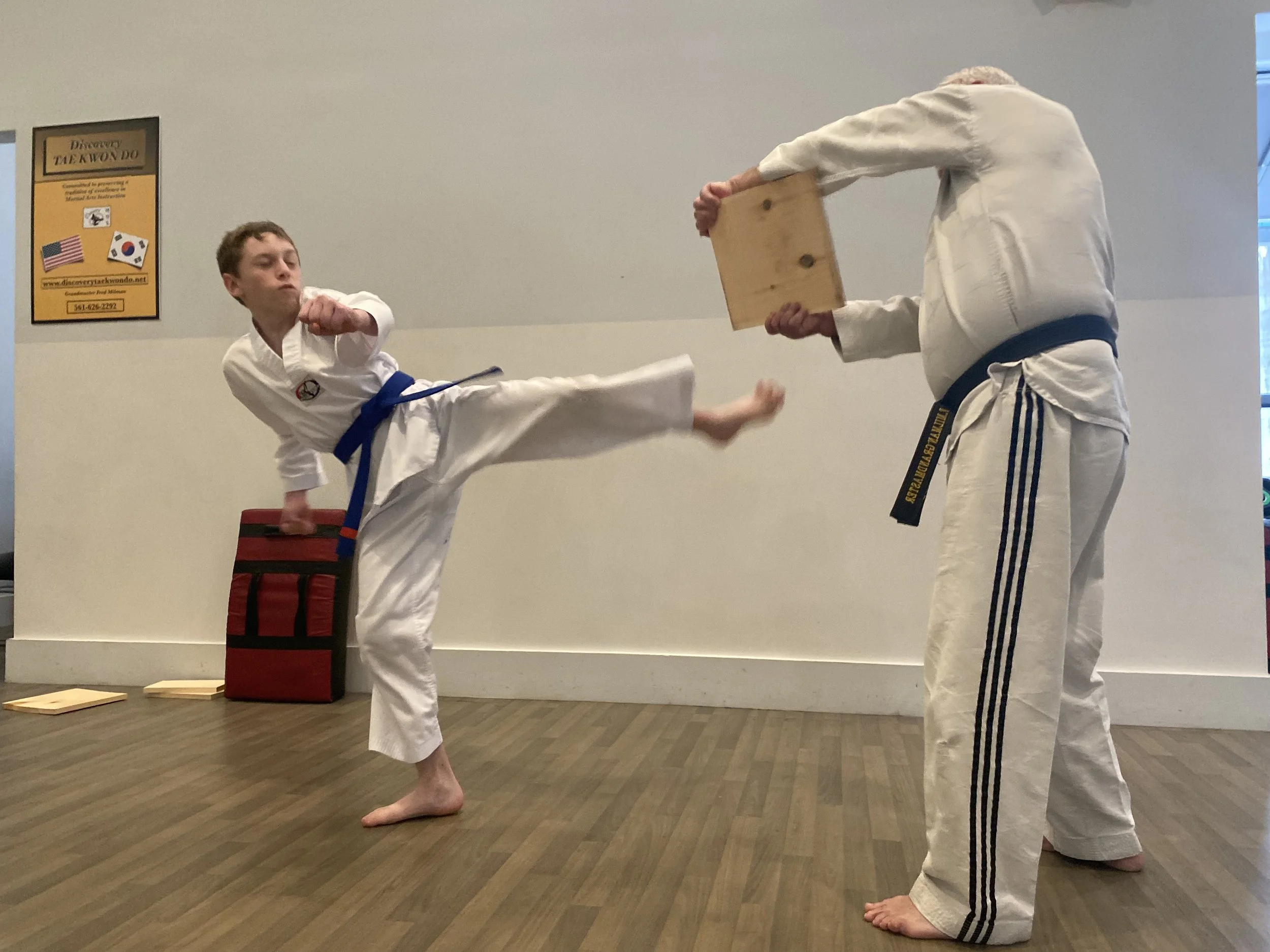 Student kicks board while Grandmaster Milman holds the board.