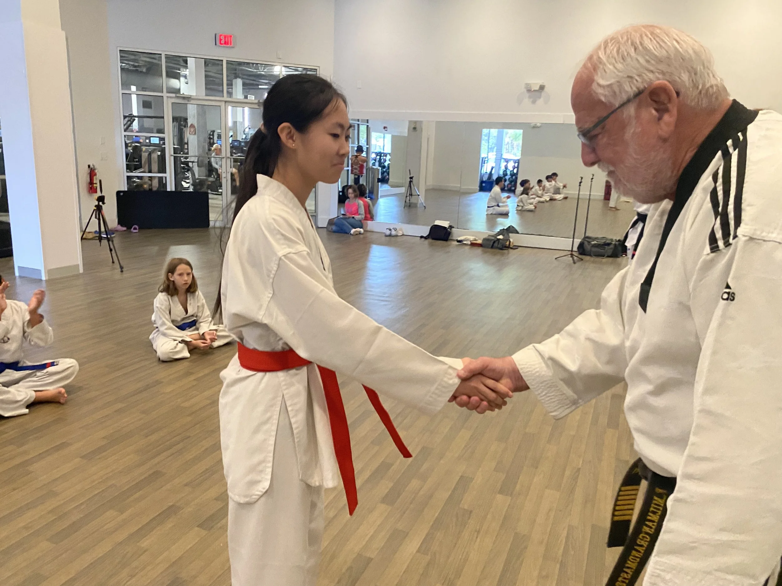 Female student with red belt shakes Grandmaster Milman's hand