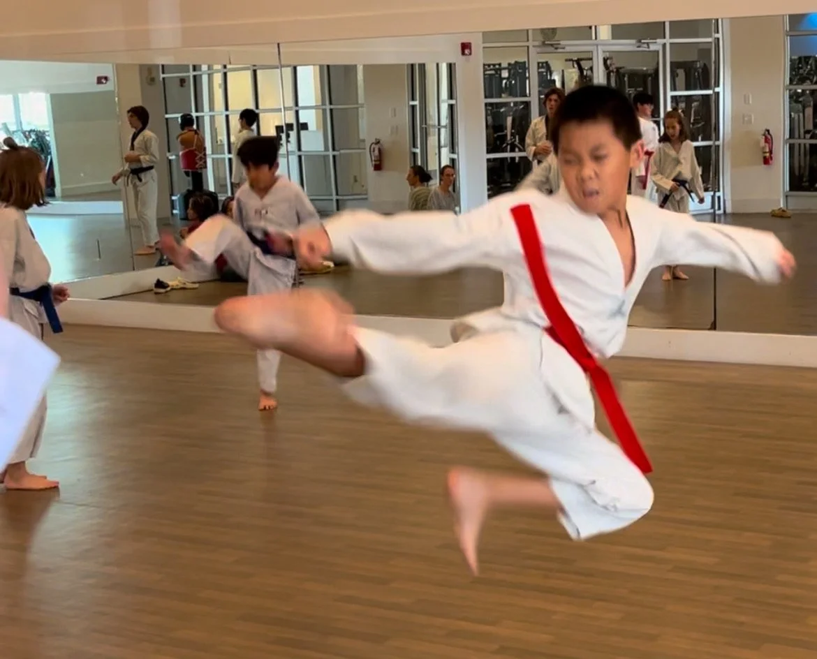 Boy with a red belt does a flying sidekick 