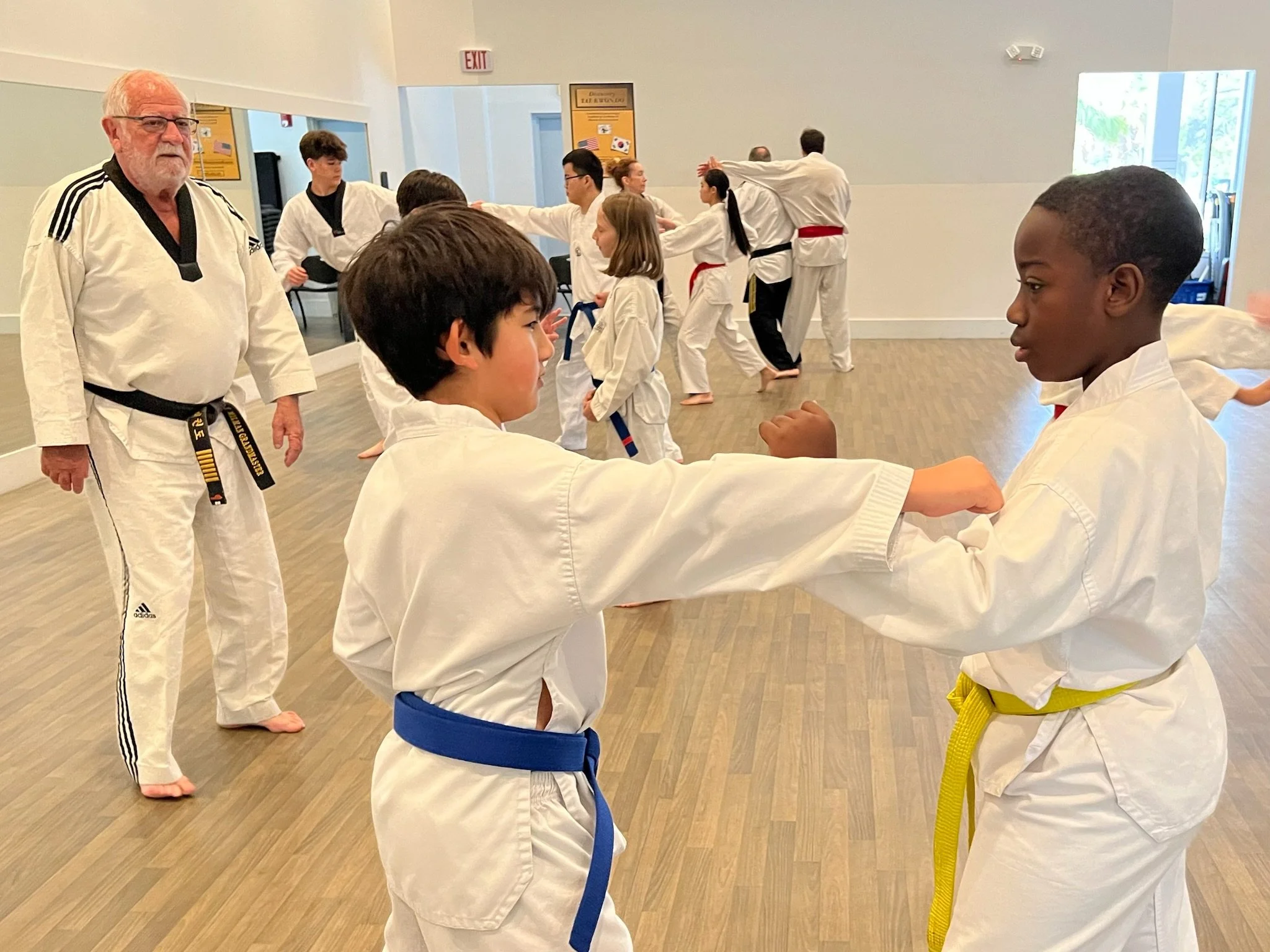 Grandmaster Milman watches two boys spar. One with a blue belt and the other with a yellow belt. 
