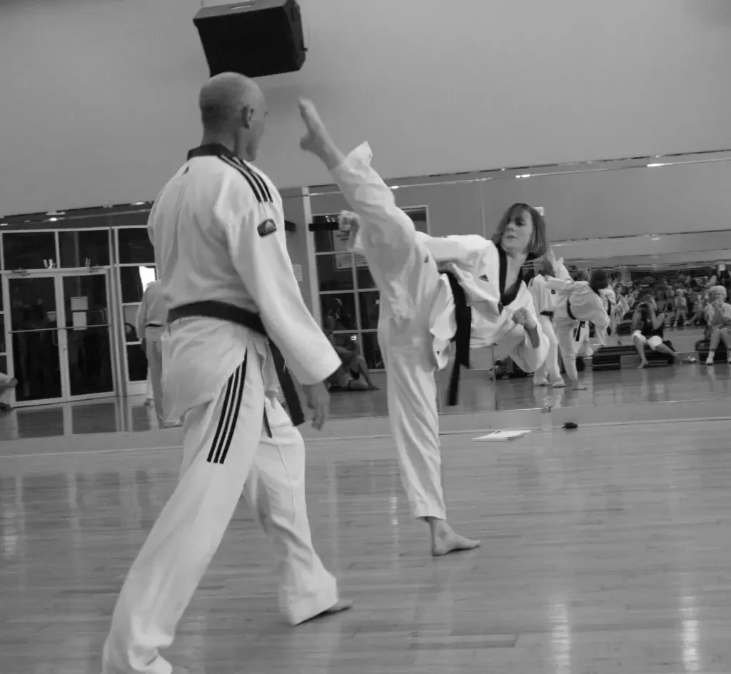 Black and white photo of a woman kicking toward a man. 