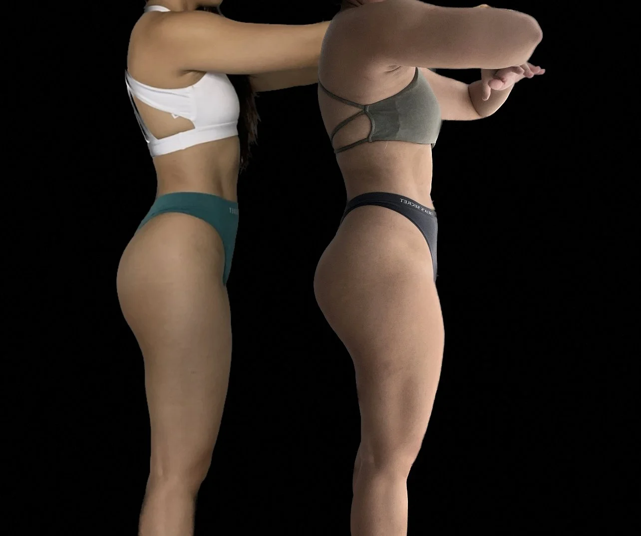 Two women in athletic underwear standing side by side against a black background, with their upper bodies not visible.