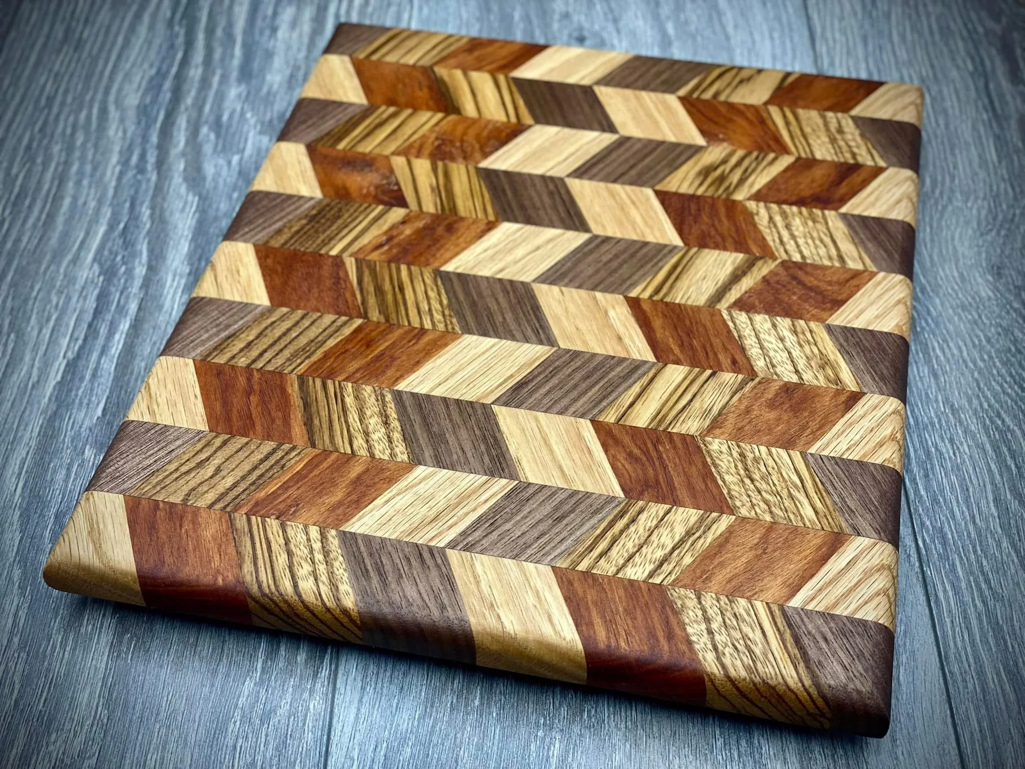 Multiple small rectangular wooden blocks with various wood grain patterns arranged in a herringbone pattern on a gray surface.