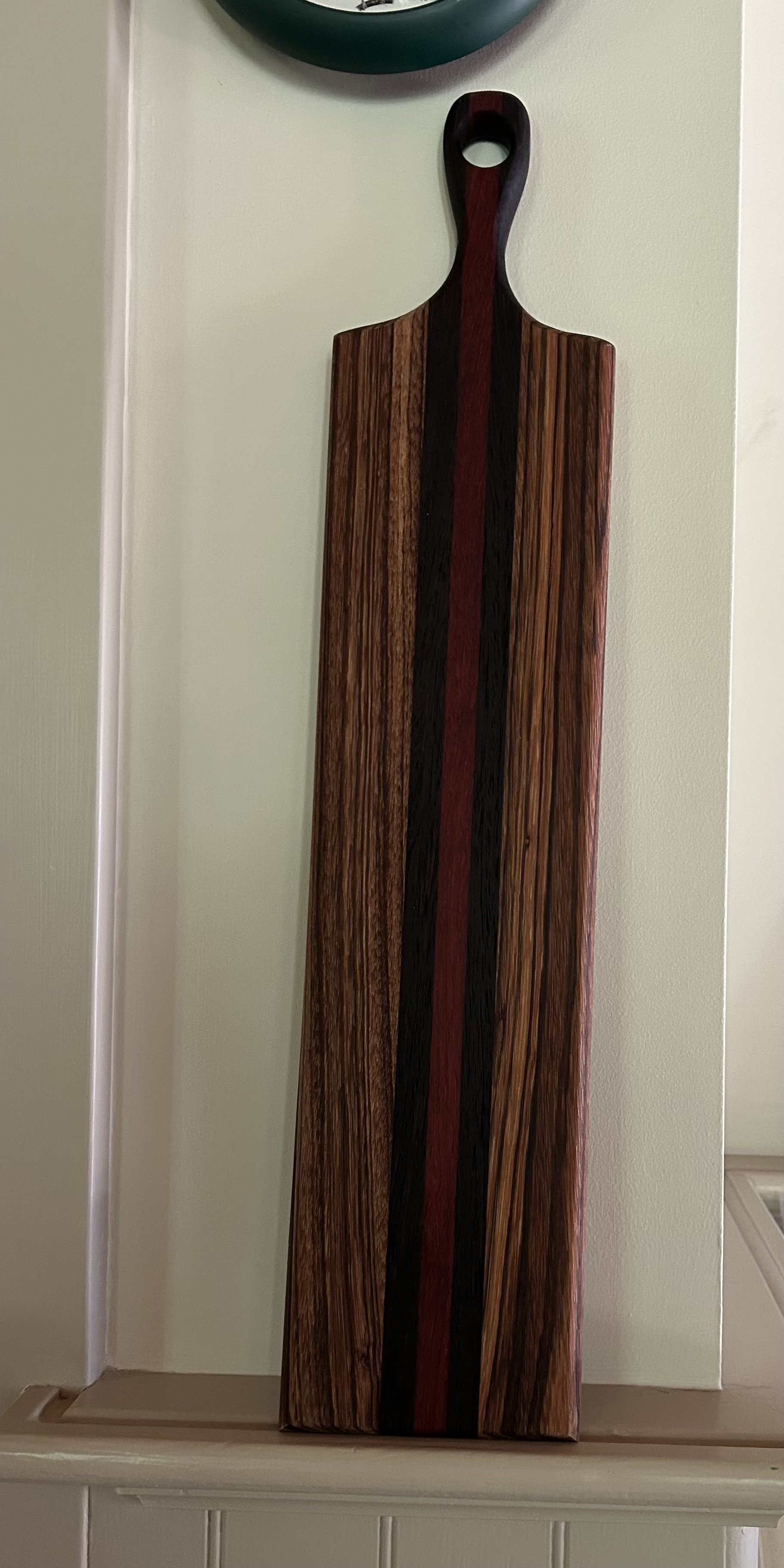 A wooden cutting board with a dark stripe down the middle and a red stripe beside it, leaning against a wall.