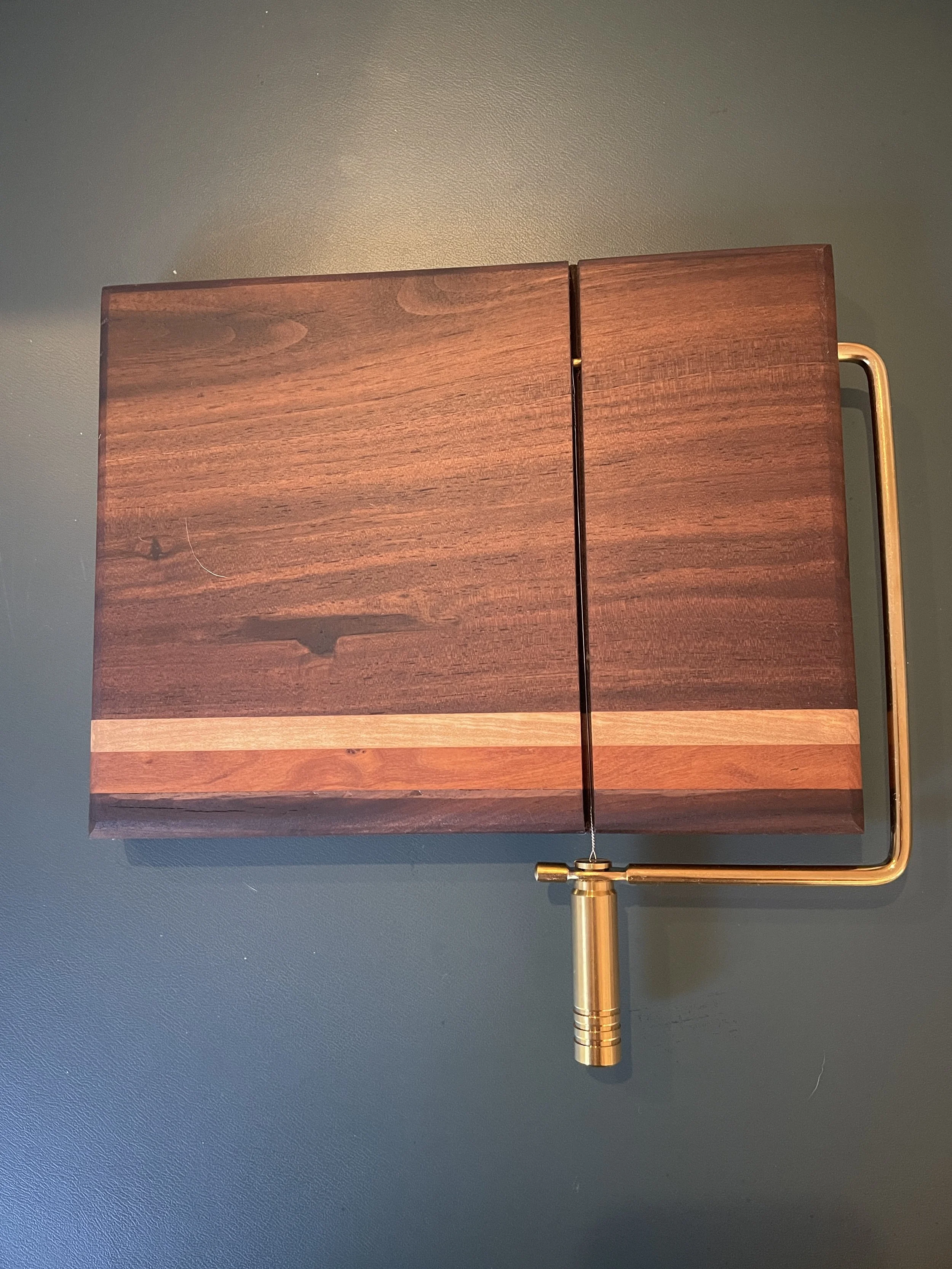 A wooden chessboard with a metal handle on the right side, resting on a dark surface.