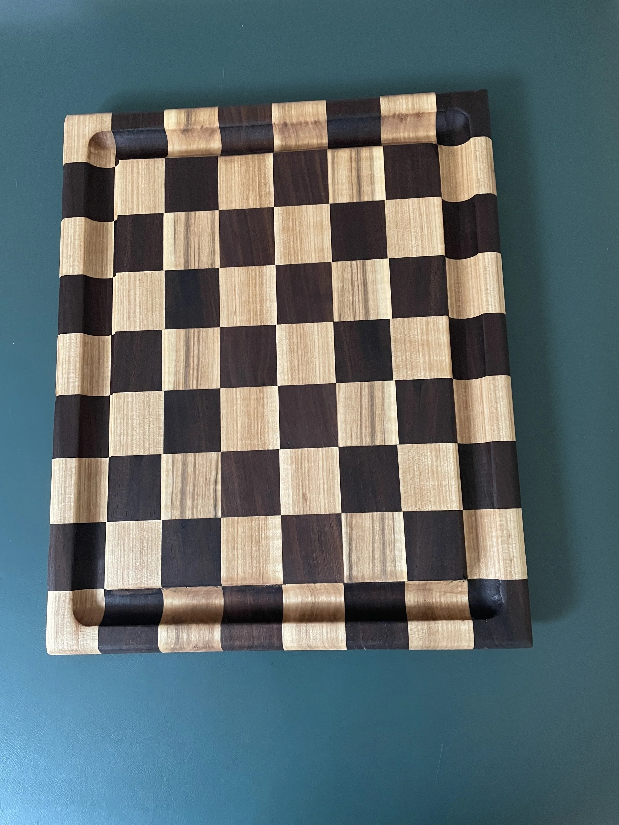 Wooden chessboard with alternating light and dark squares, placed on a teal surface.