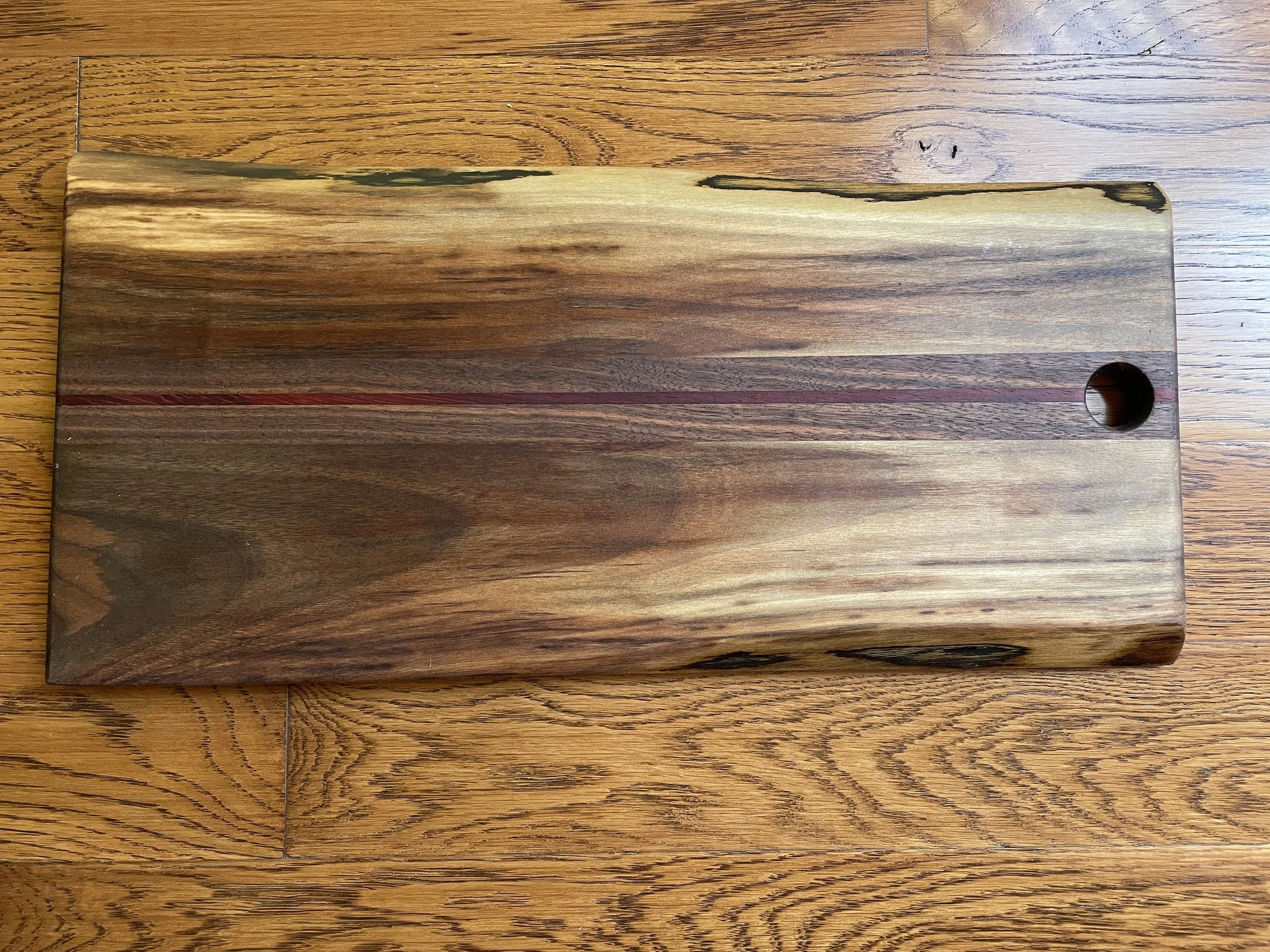 A wooden cutting board with a circular hole in one corner, placed on a wooden table.