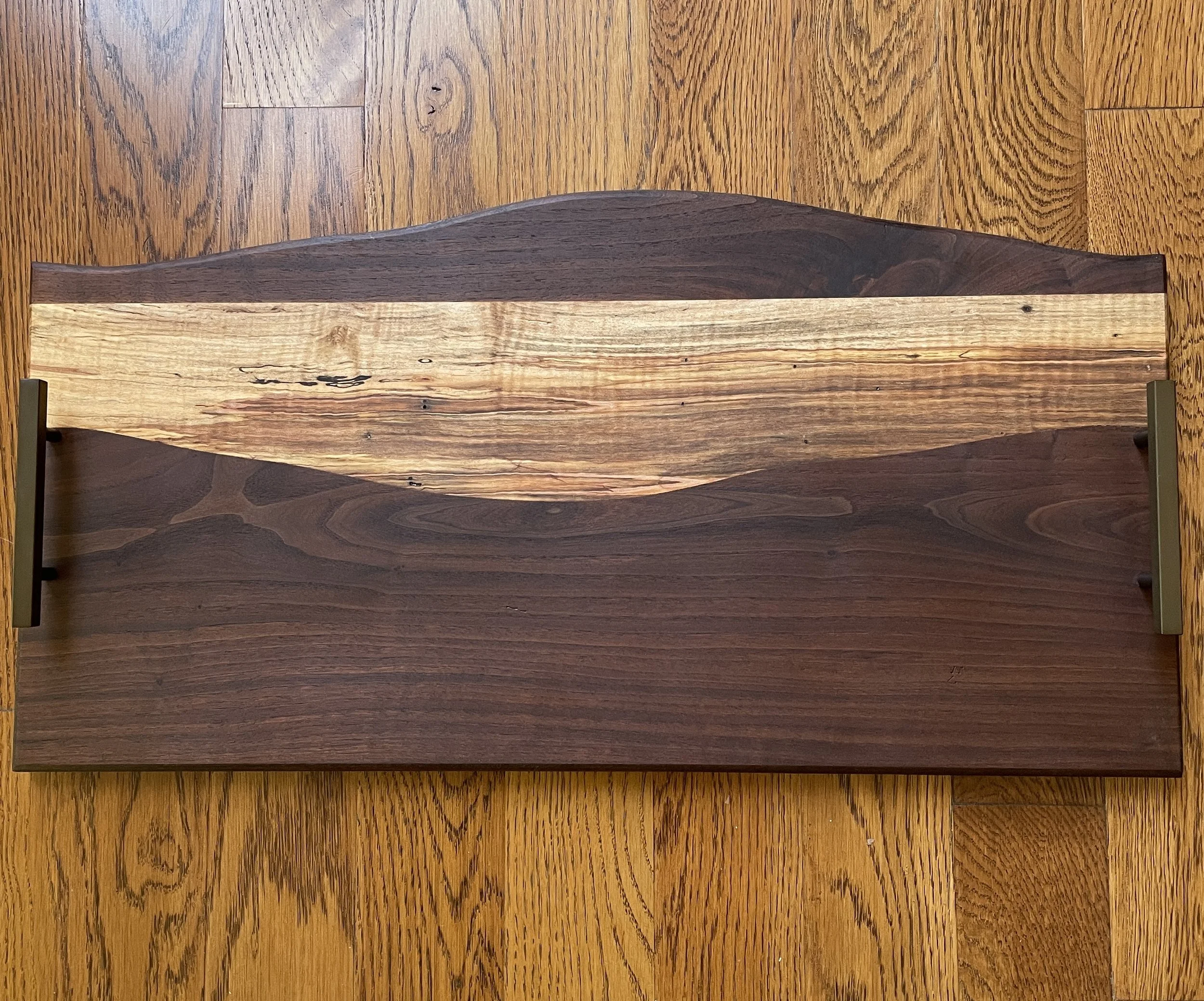 A rectangular wooden tray with a natural finish, featuring a darker, curved design on a lighter wood section, resting on a wooden surface.