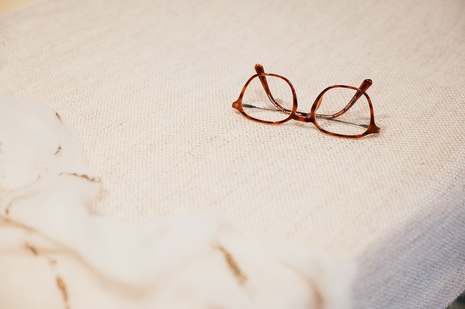 A pair of brown tortoise shell glasses resting on a textured cream-colored surface.