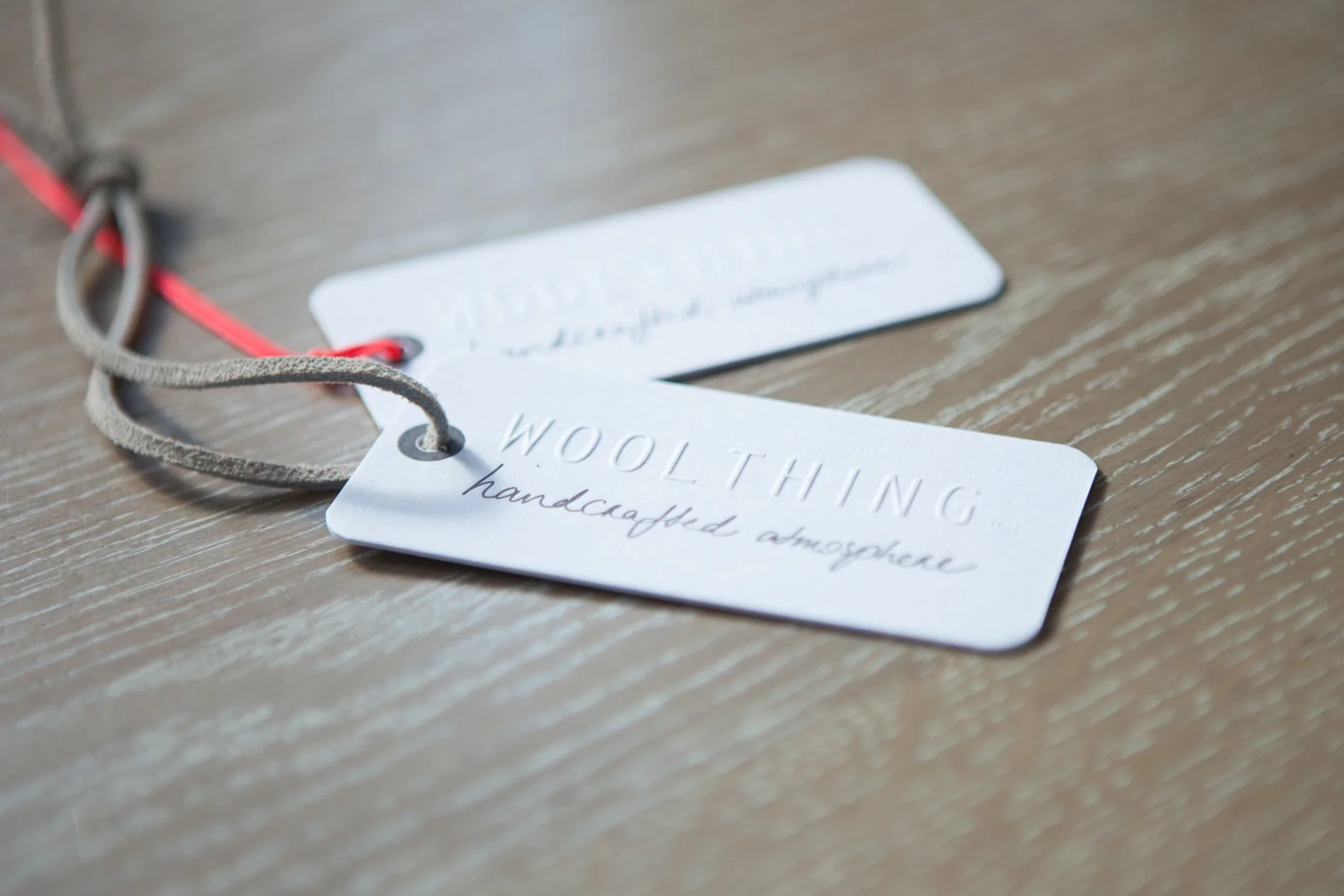 Close-up of a wool tag with the text 'WOOLTHING handcrafted atmosphere' lying on a wooden surface.