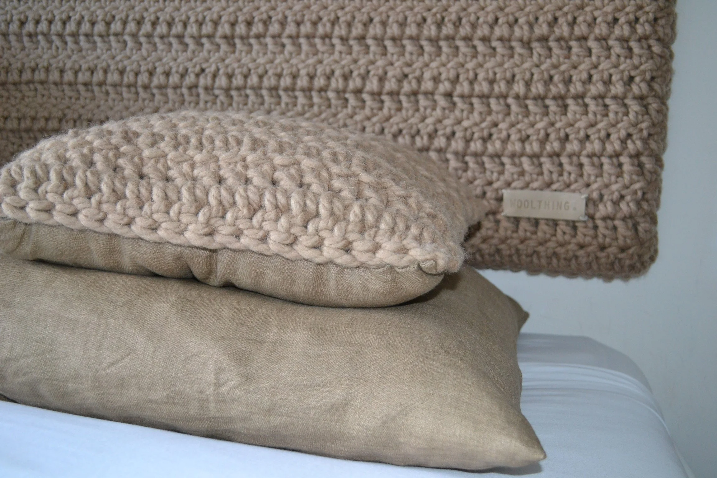 A close-up of beige textured pillows, including a chunky knit pillow, on a bed with white sheets.
