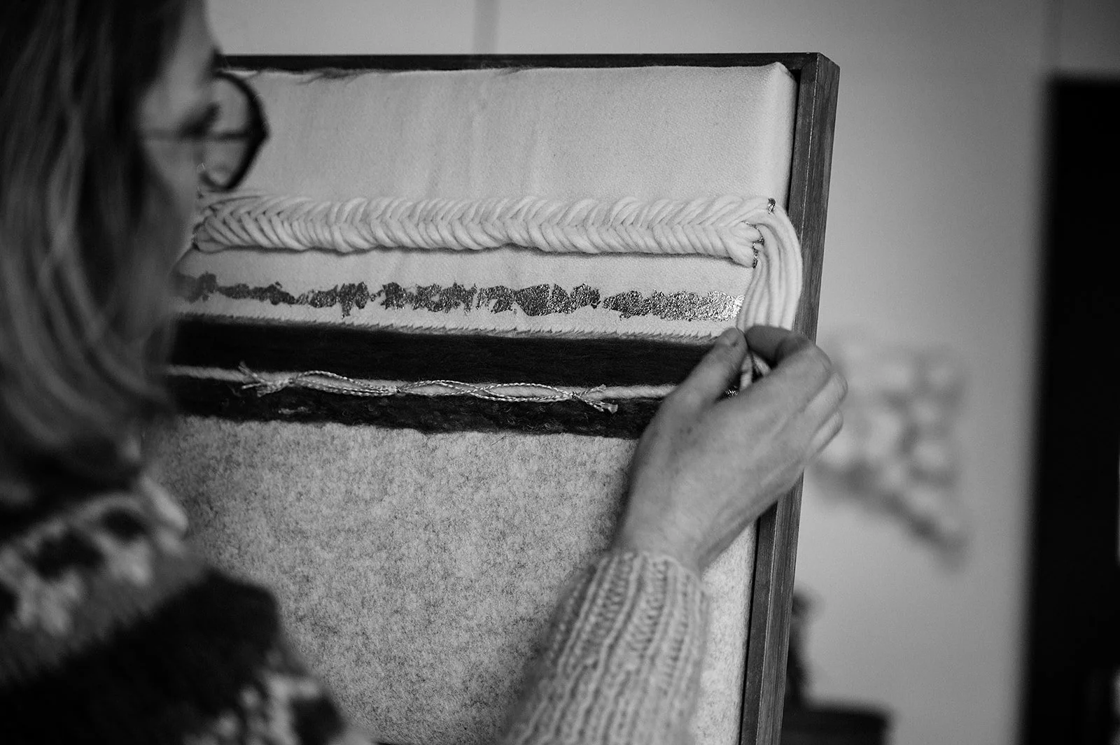 A person weaving a piece of fabric on a loom, with close-up focus on their hands and the woven material.