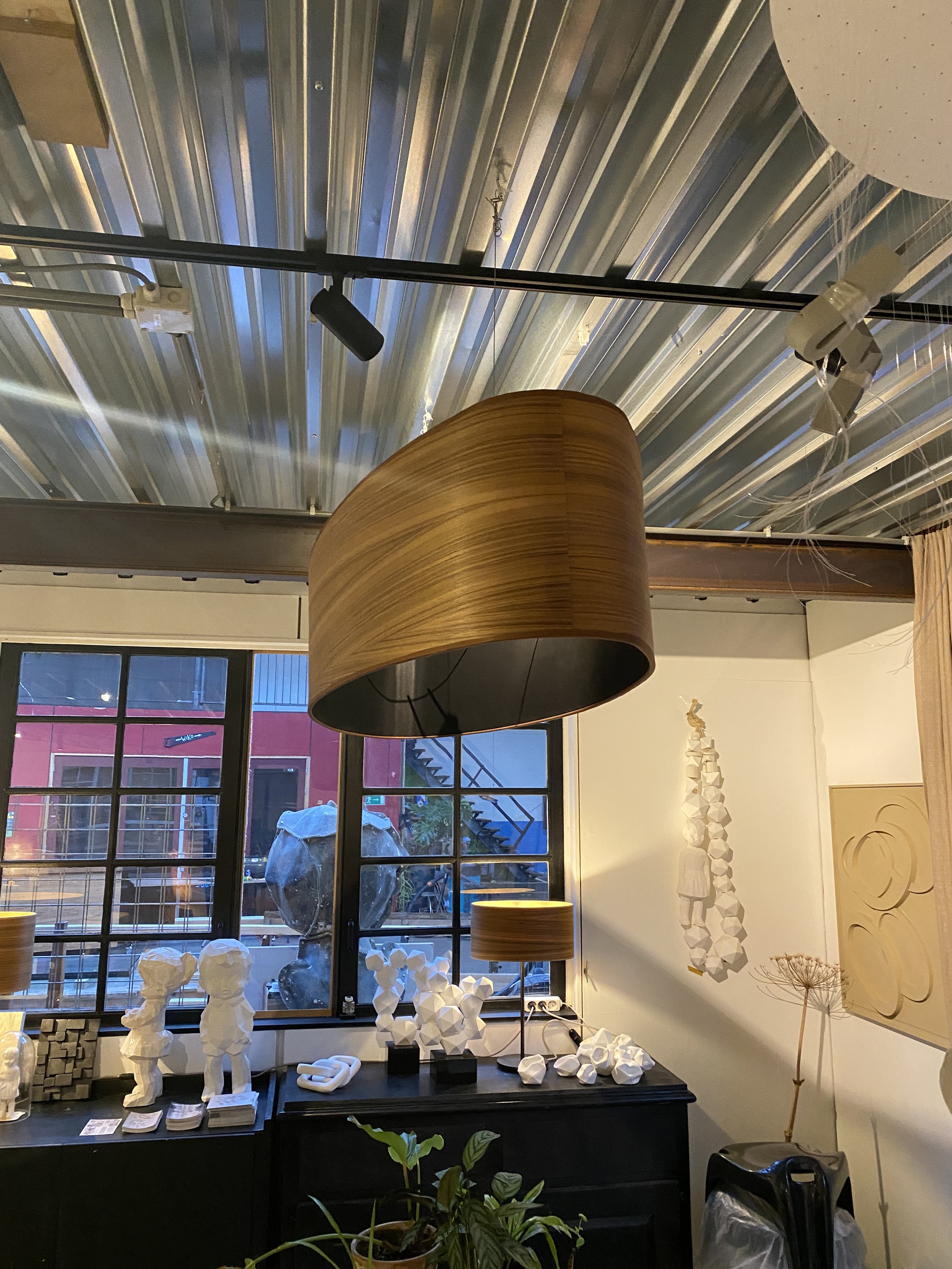 Interior of a modern home or gallery with decorative sculptures, a large wooden lampshade, and artworks on the walls, with a large window showing an outdoor scene.