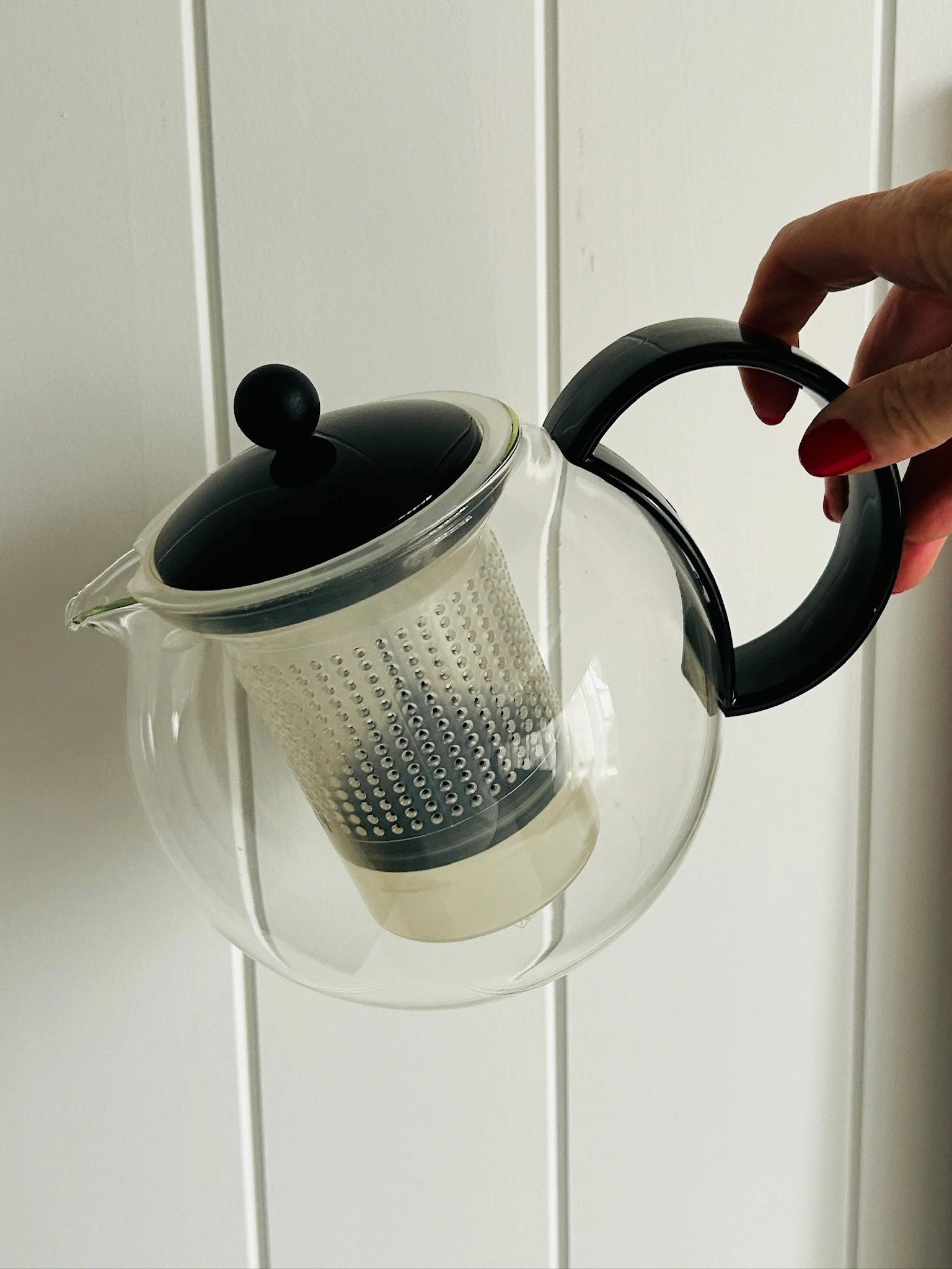 Angled view of the Bodum Assam teapot held in hand, highlighting the pouring spout, suspended infuser, and curved black handle.