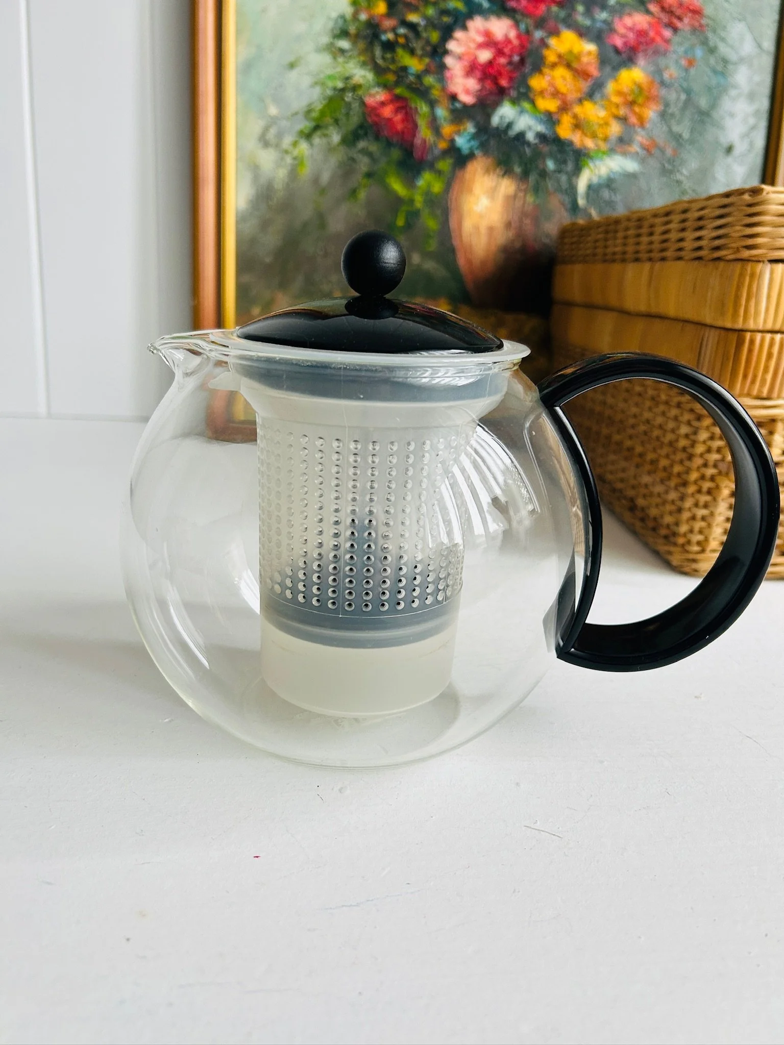 Front view of vintage Bodum Assam tea press in clear borosilicate glass with black lid, black handle, and white mesh infuser inside.