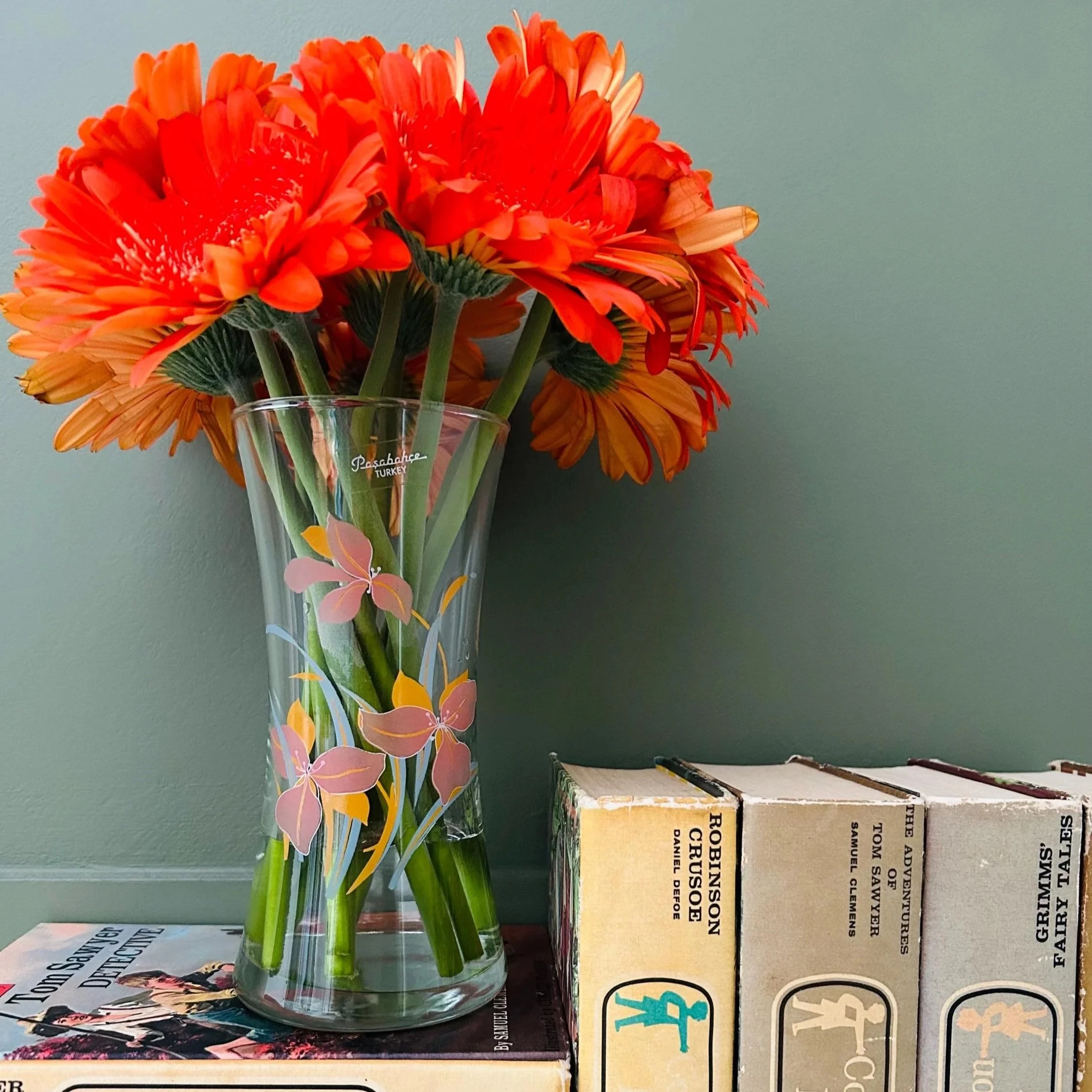 Vase styled with bright orange flowers beside retro packaging