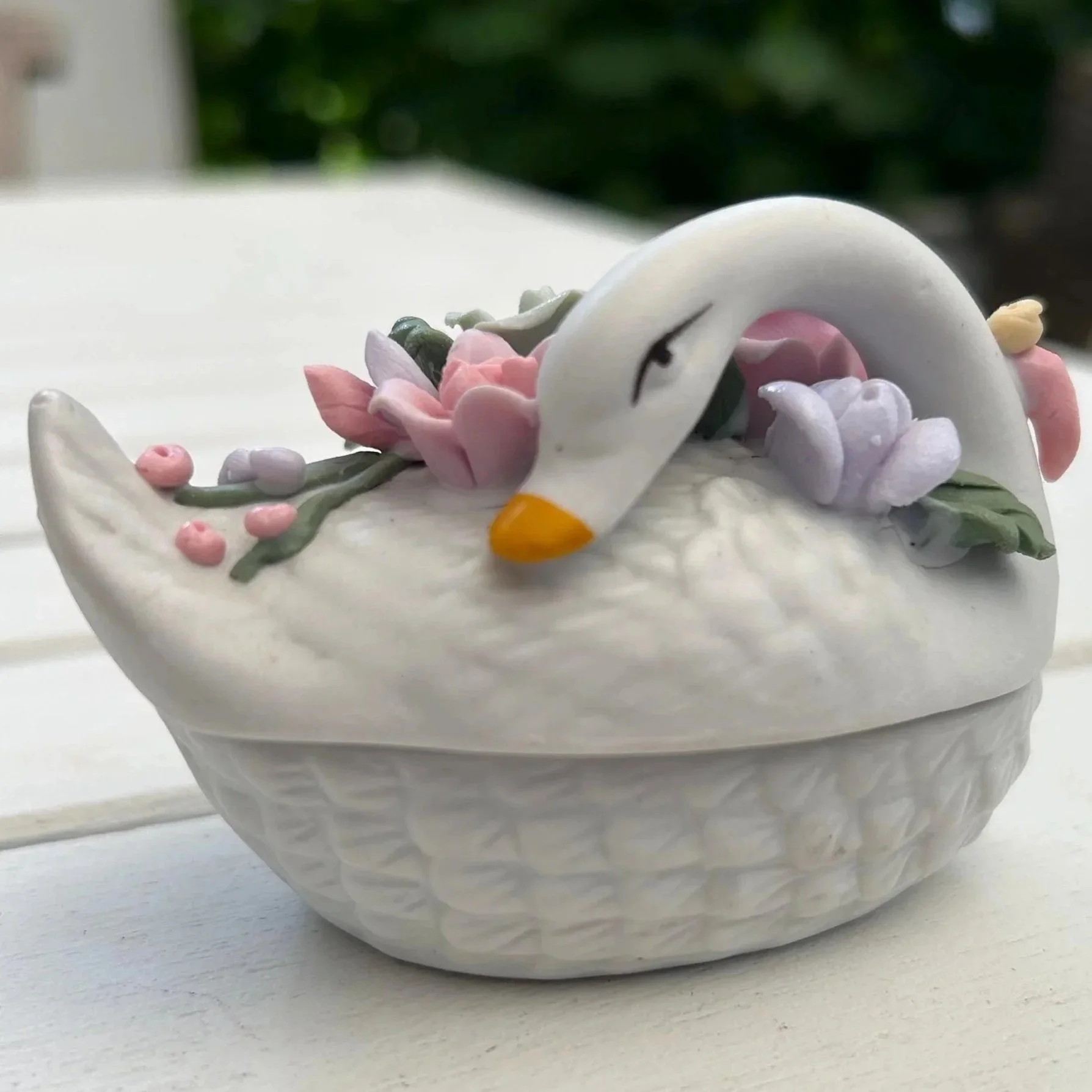 Side view of porcelain swan trinket box with lid closed, showing floral top and orange beak