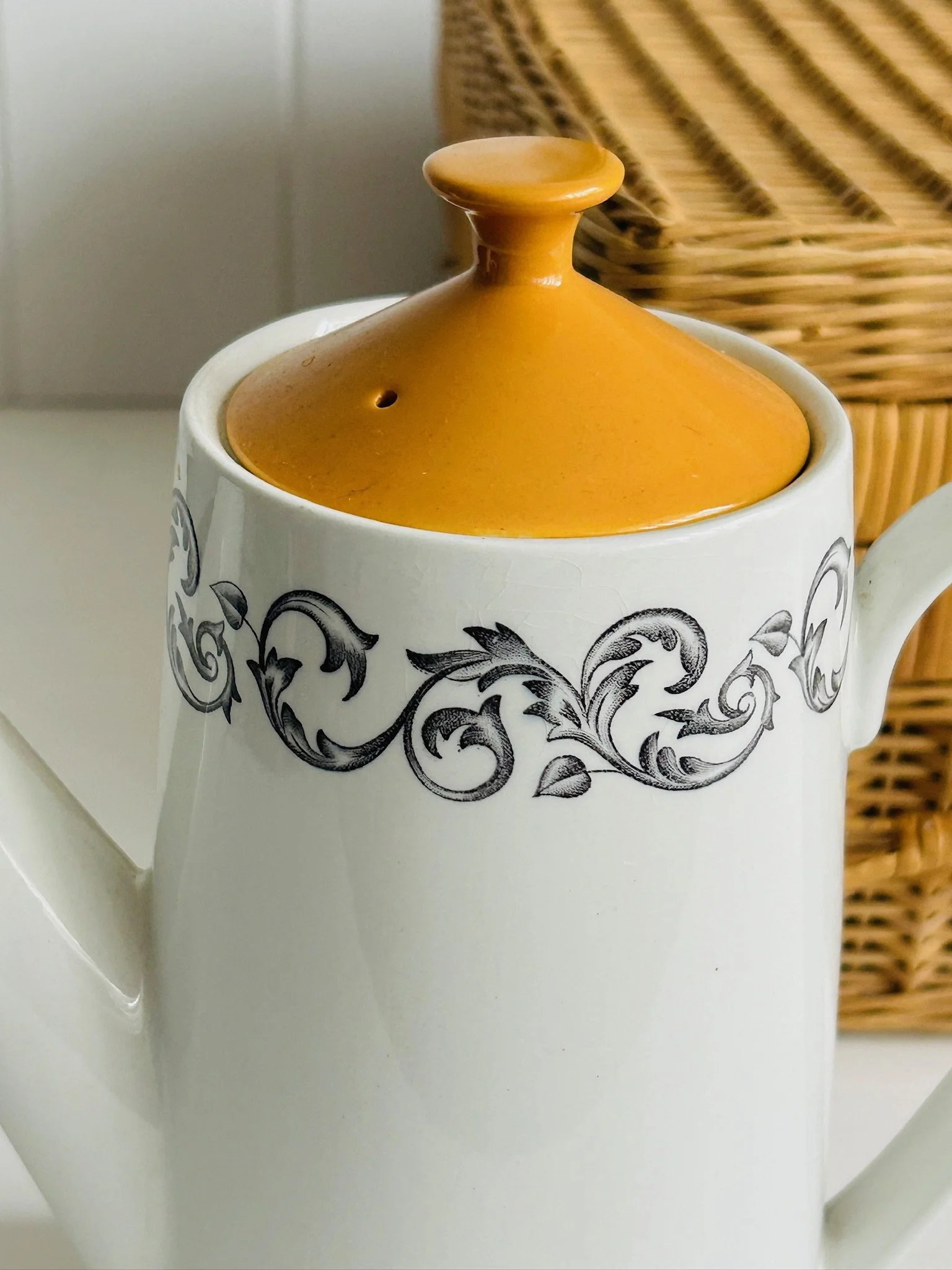 Close-up of the upper body and lid, showing the vivid orange lid, finial detail, and black baroque scrollwork pattern around the rim.