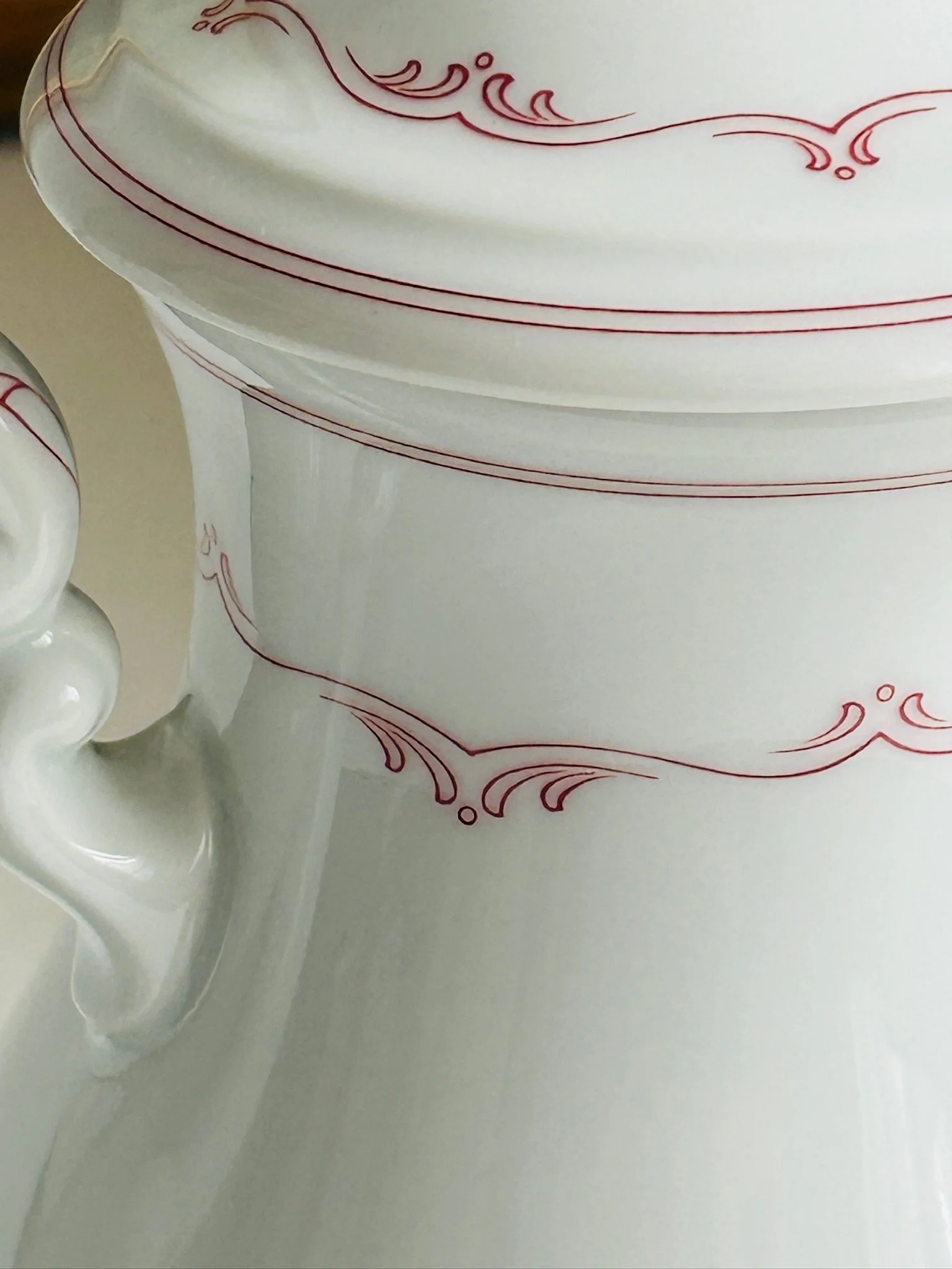 Close-up of the body pattern and handle area, showing the fine red scroll motif on glossy white porcelain.