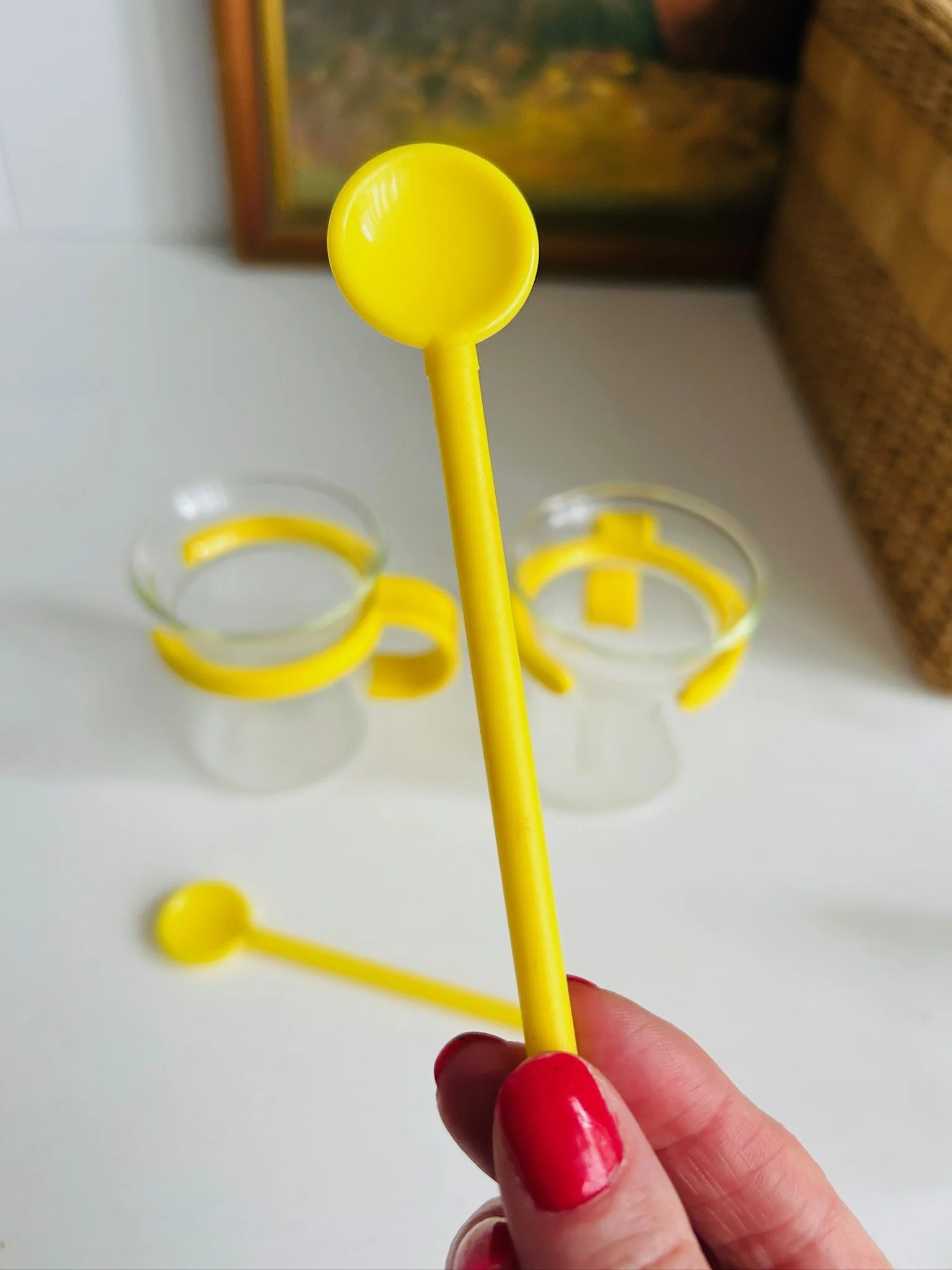 Close-up of a yellow Bodum spoon held in hand, with matching yellow-handled glass cups softly blurred in the background.