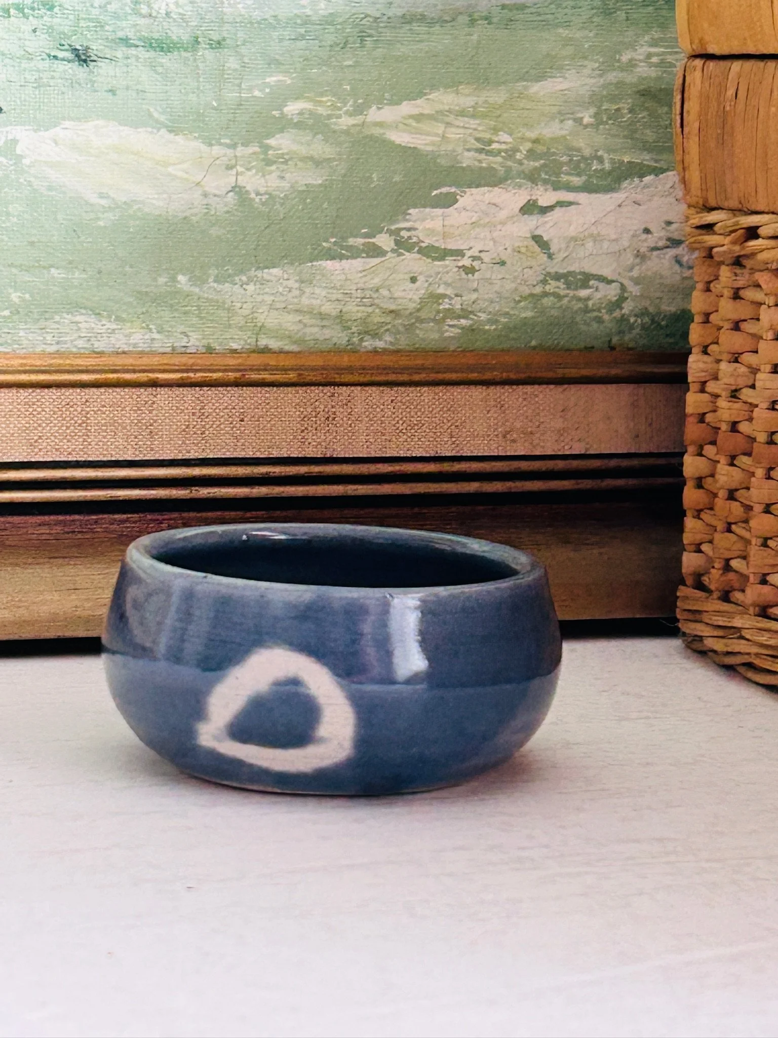 Styled display view of the small studio pottery bowl resting on a white surface in front of framed artwork